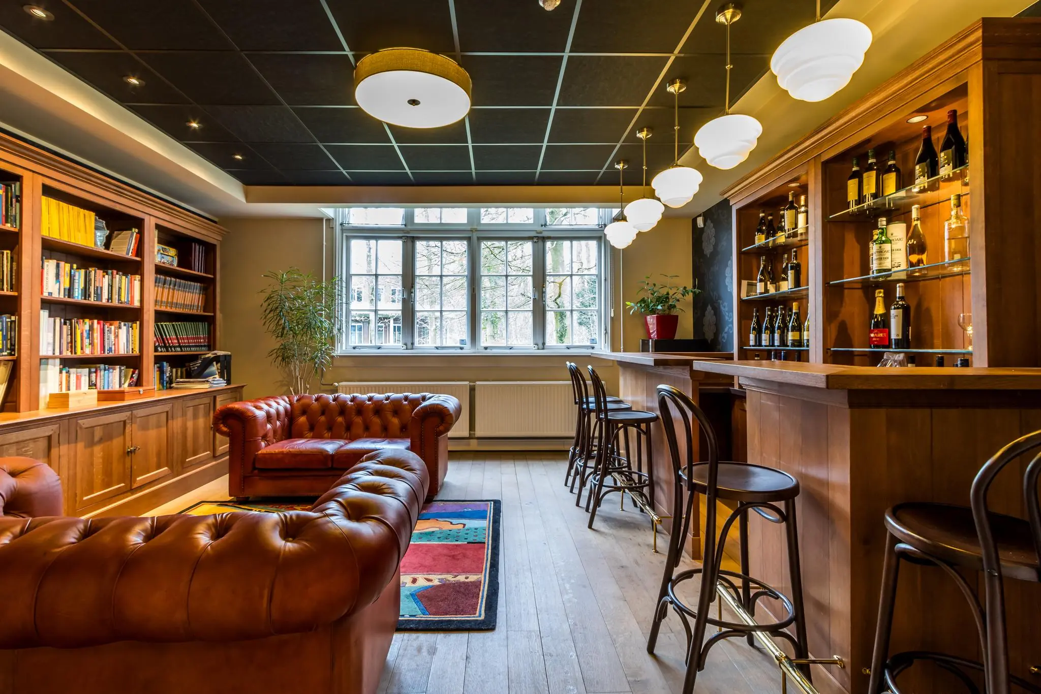 Sfeervolle bibliotheek met leren Chesterfieldbanken, een houten bar en gevulde boekenkasten aan de Driebergseweg.