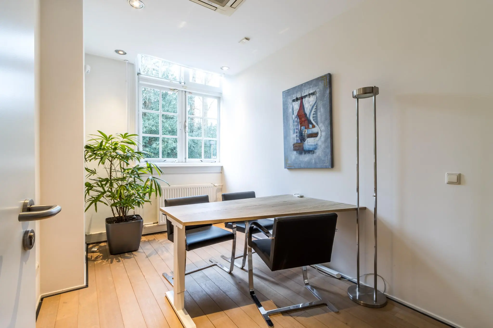 Modern ingerichte vergaderruimte aan de Driebergseweg met een houten tafel, vier stoelen, kamerplant en schilderij aan de muur.