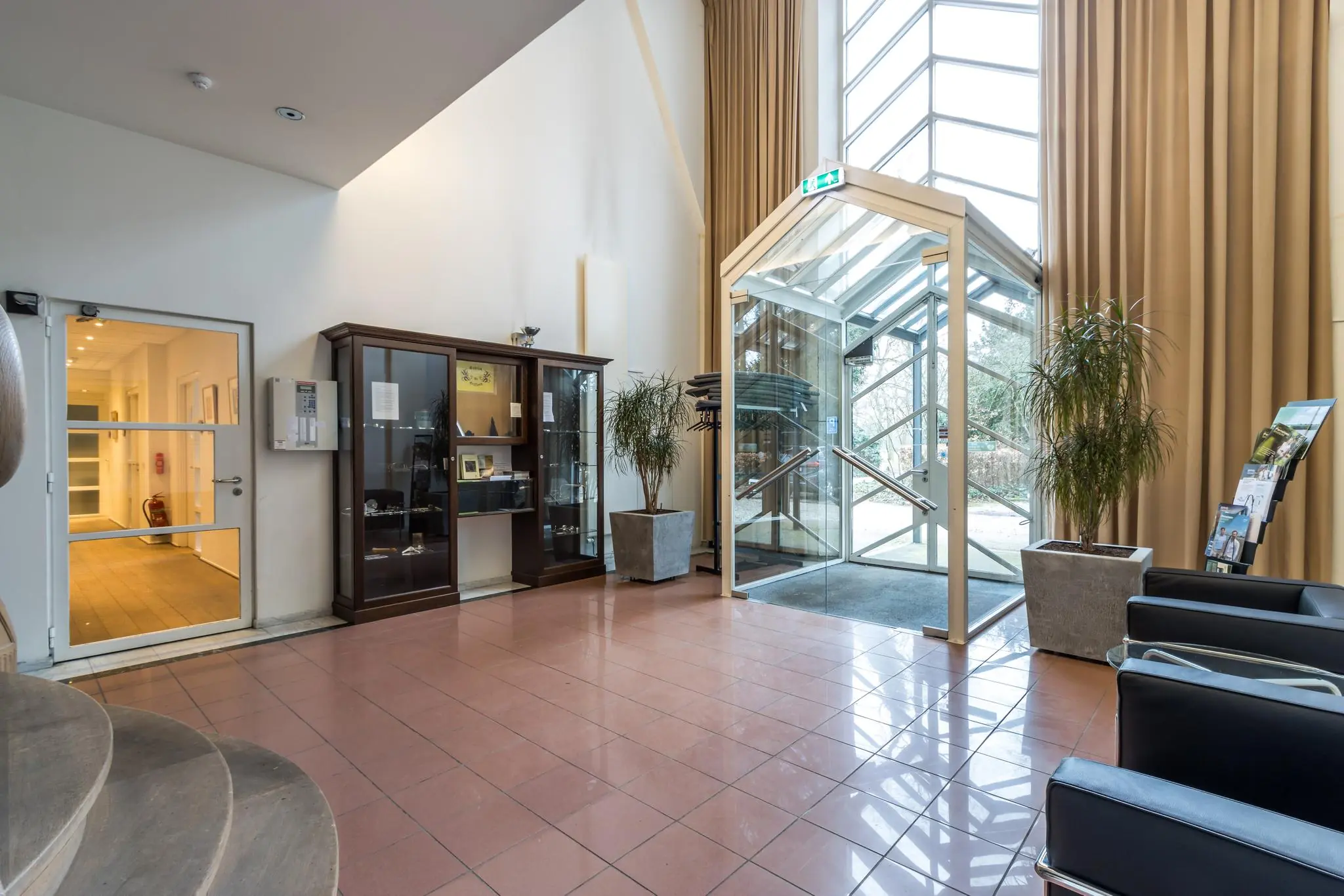 Ingang en ontvangsthal van een gebouw aan de Driebergseweg met glazen deuren, vitrinekast en wachtruimte.