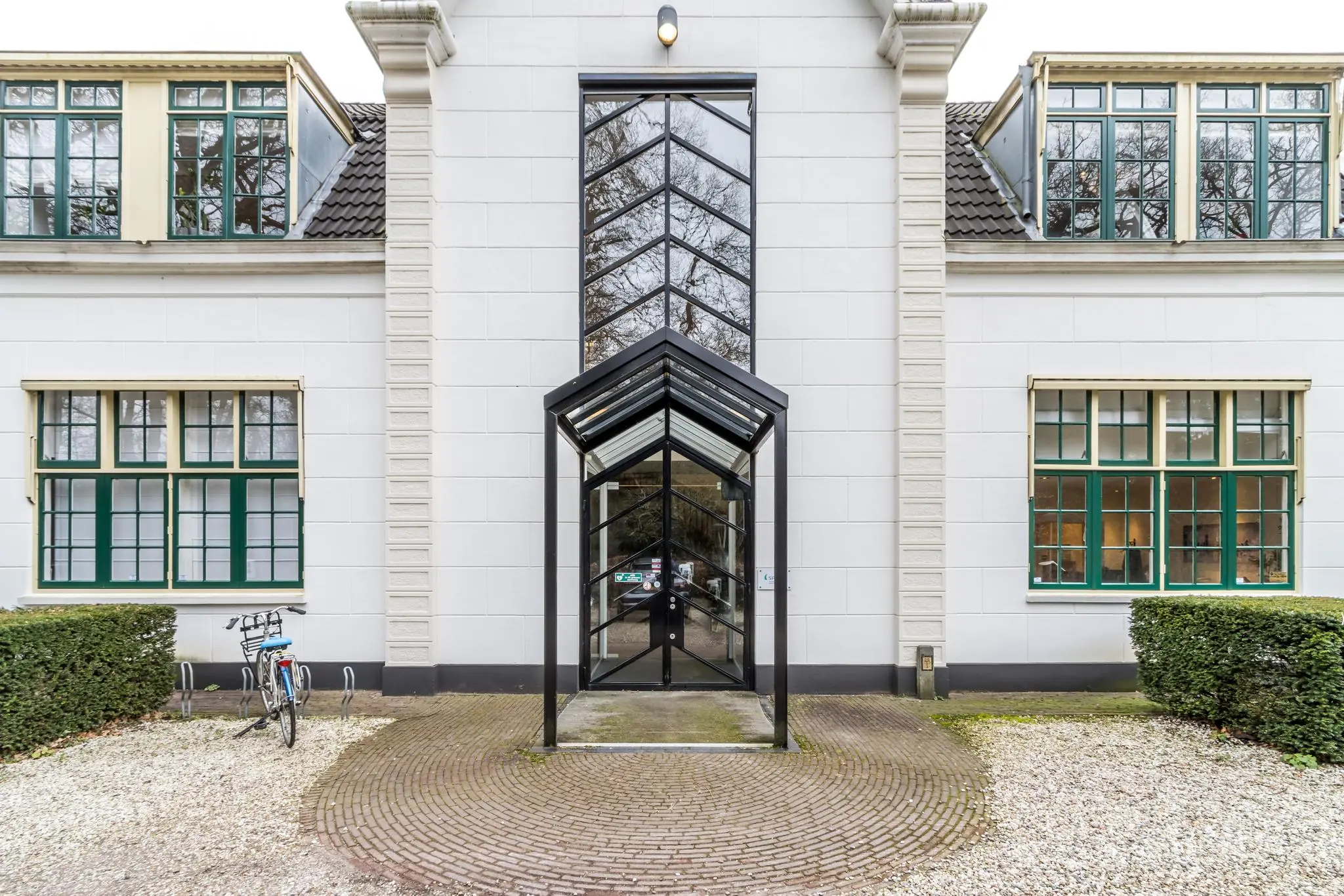 Moderne entree met glazen overkapping van een wit kantoorpand aan de Driebergseweg.