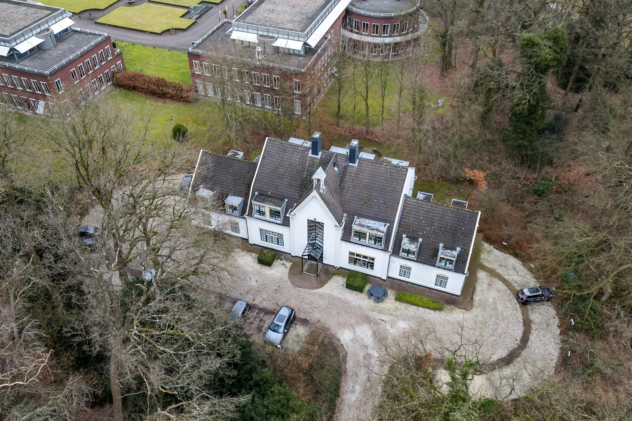 Luchtfoto van een groot wit herenhuis aan de Driebergseweg, omringd door bomen en moderne kantoorgebouwen.
