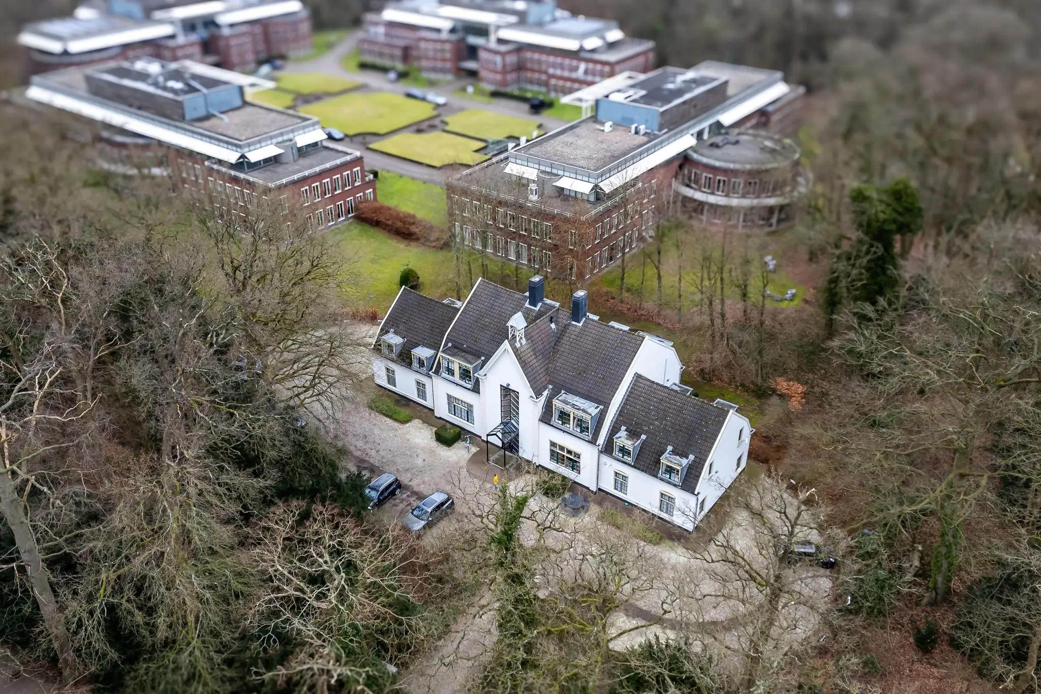 Luchtfoto van een wit herenhuis aan de Driebergseweg, omringd door bomen en grotere kantoorgebouwen.