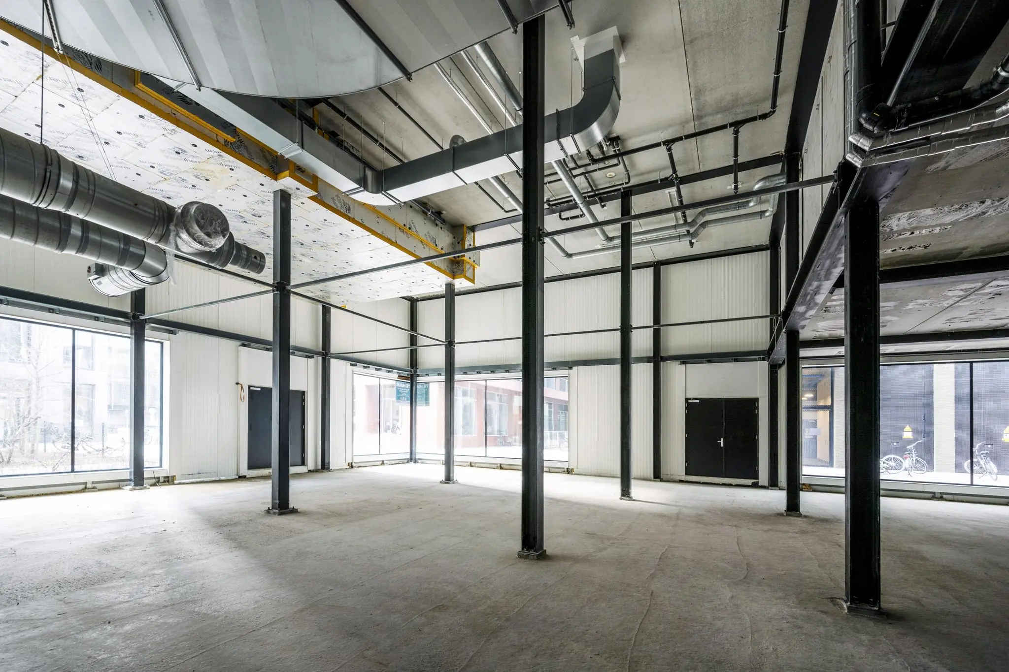 Leeg bedrijfs- of winkelpand aan de Pieter Goosstraat met betonnen vloer, hoge plafonds en zichtbare ventilatiebuizen.