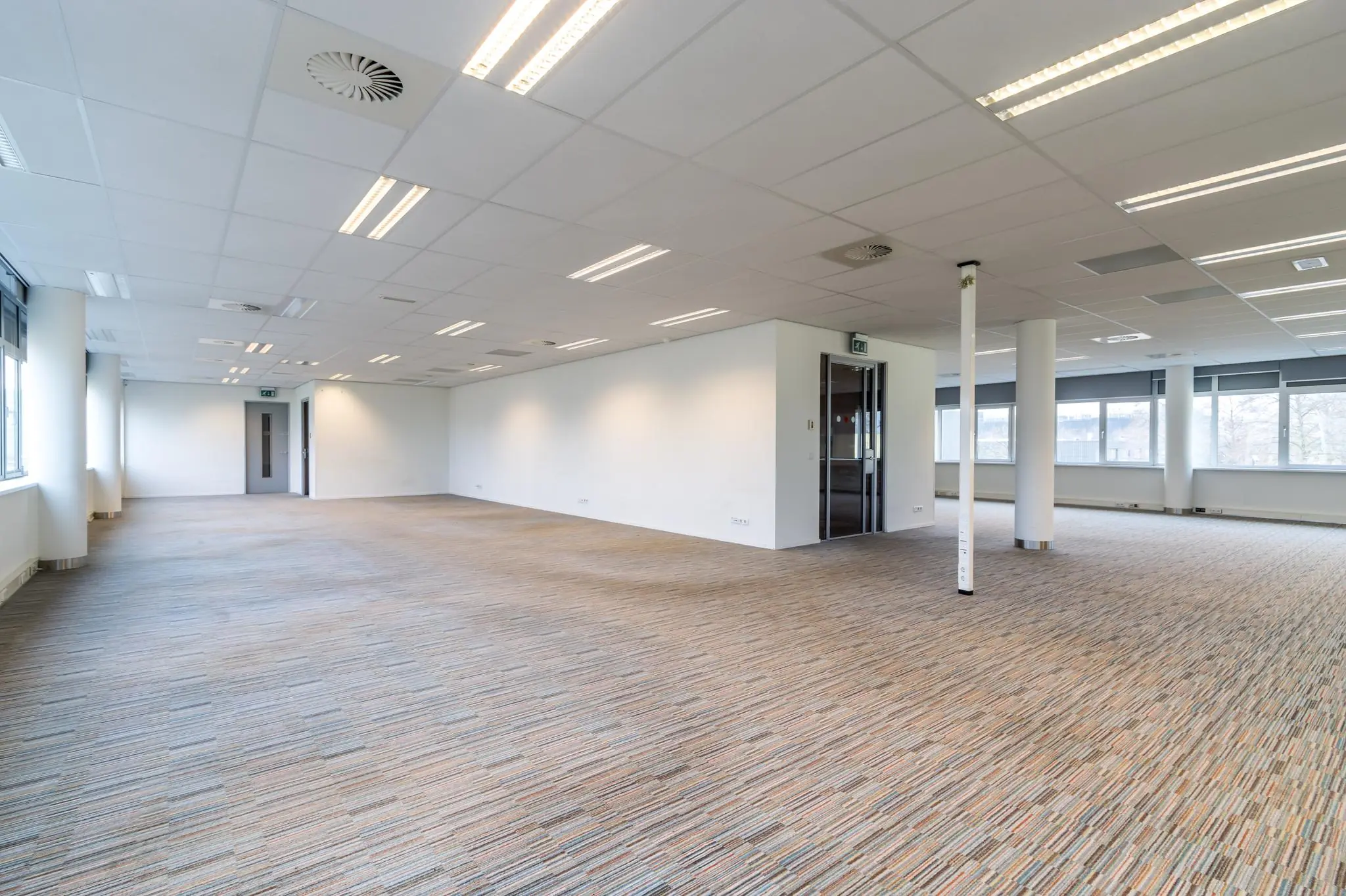Leeg en modern kantoorpand aan de Lemelerbergweg met tapijtvloer, systeemplafond en grote ramen.