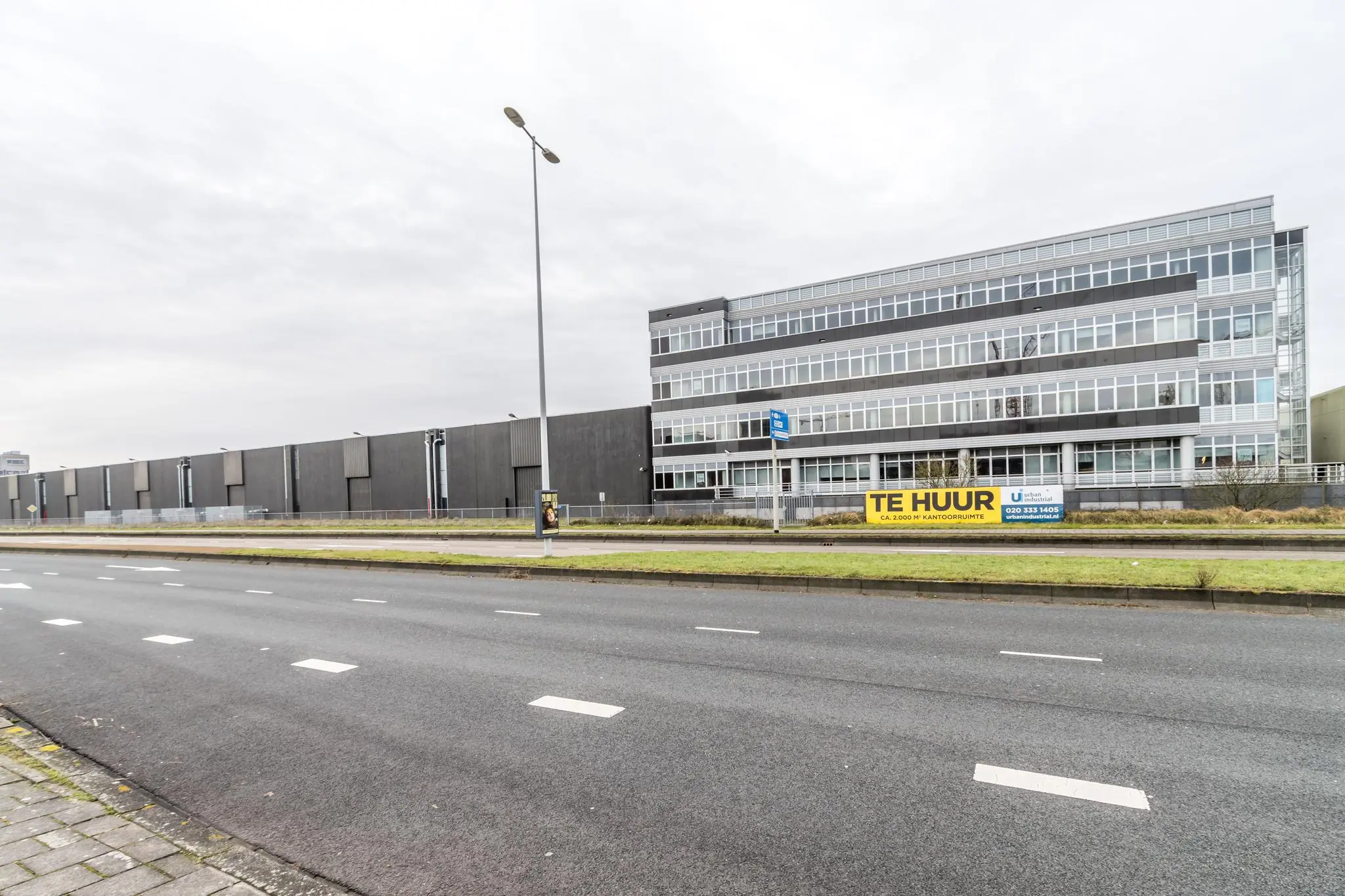 Kantoorpand aan de Lemelerbergweg met een groot "Te Huur"-bord langs een brede weg.
