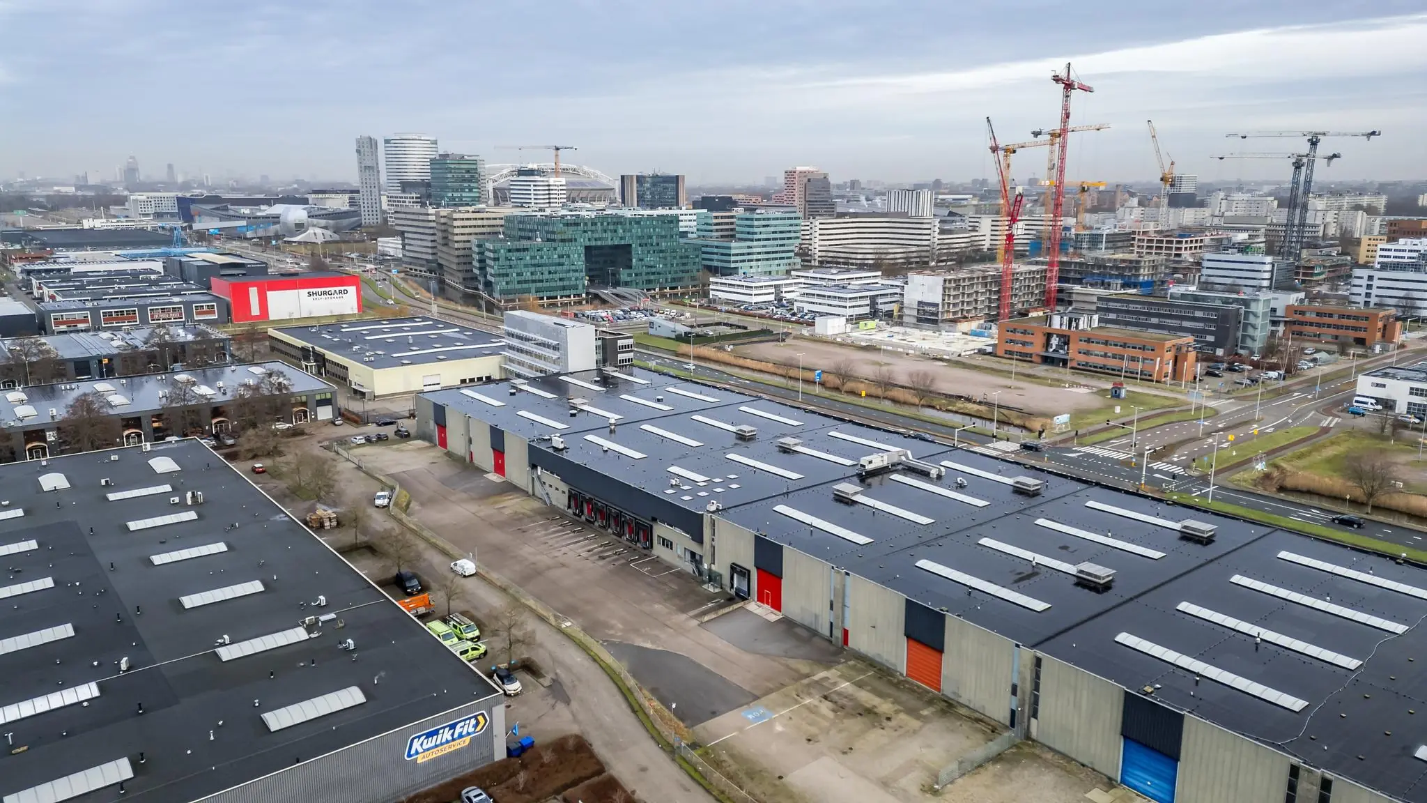 Luchtfoto van bedrijventerrein aan de Lemelerbergweg in Amsterdam met magazijnen, kantoren en bouwkranen op de achtergrond.