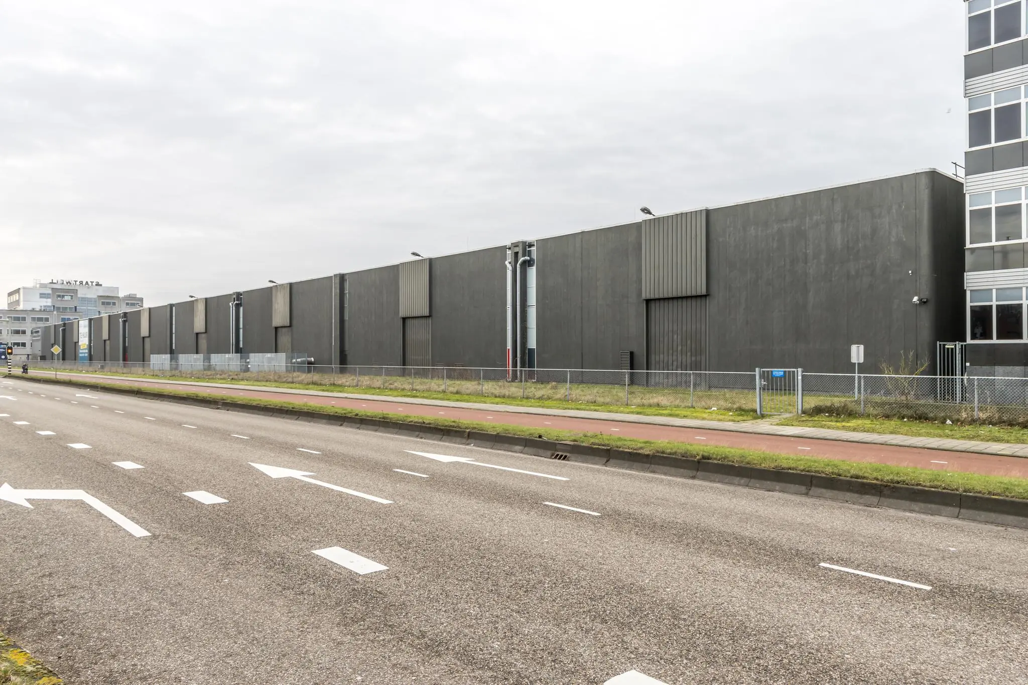 Grijze industriële loods aan de Lemelerbergweg in Amsterdam, gezien vanaf de straatzijde.