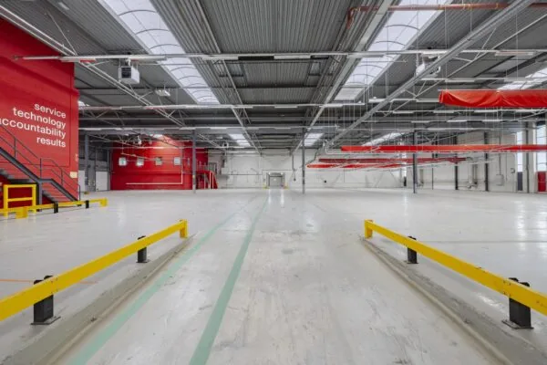 Ruime, lege bedrijfshal aan de Lemelerbergweg met rode accenten, gele veiligheidsbarrières en teksten op een rode muur.