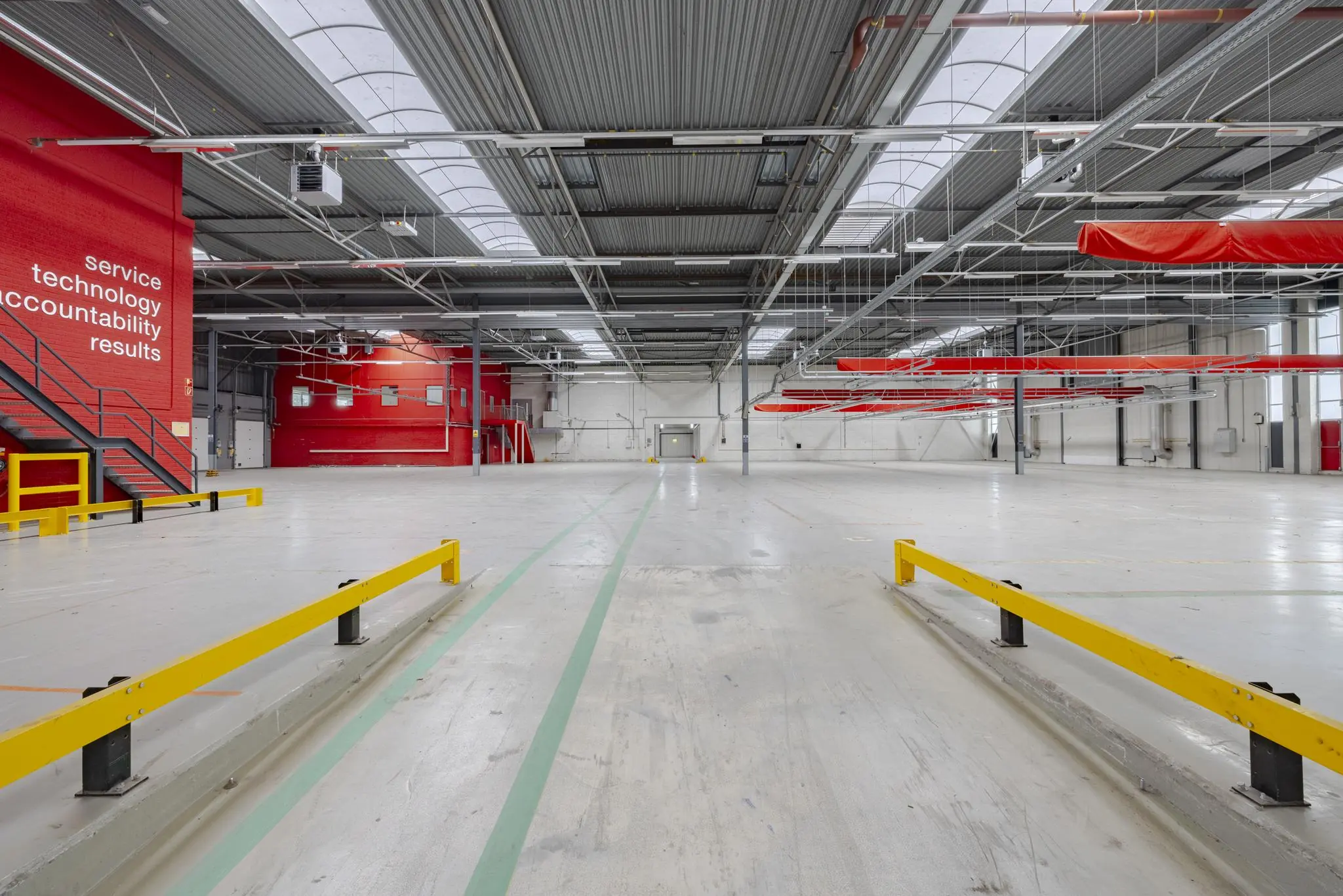 Ruime, lege bedrijfshal aan de Lemelerbergweg met rode accenten, gele veiligheidsbarrières en teksten op een rode muur.