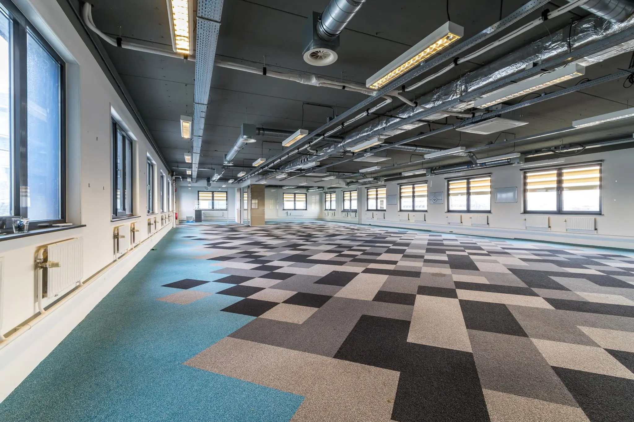 Moderne, lege kantoorruimte aan de Laarderhoogtweg met kleurrijk patroon op de vloer en industriële plafonduitwerking.