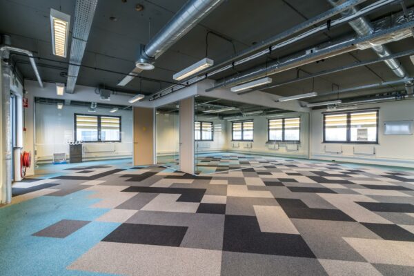 Moderne, lege kantoorruimte aan de Laarderhoogtweg met een kleurrijk patroonvloer, glazen wanden en zichtbare plafondinstallaties.
