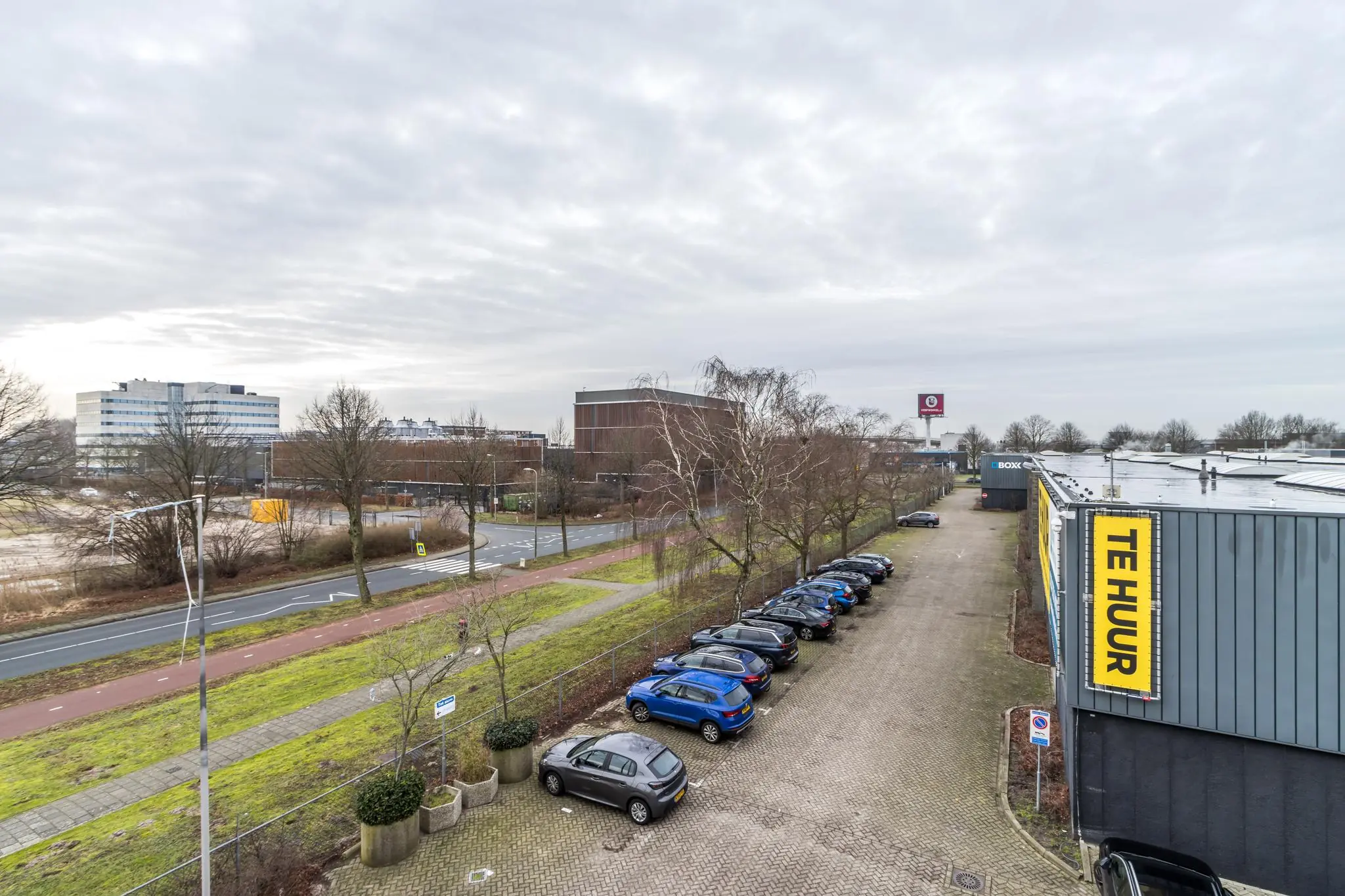 Bedrijventerrein aan de Laarderhoogtweg met parkeerplaats, kantoorpanden en een gevel met een groot "Te Huur" bord.