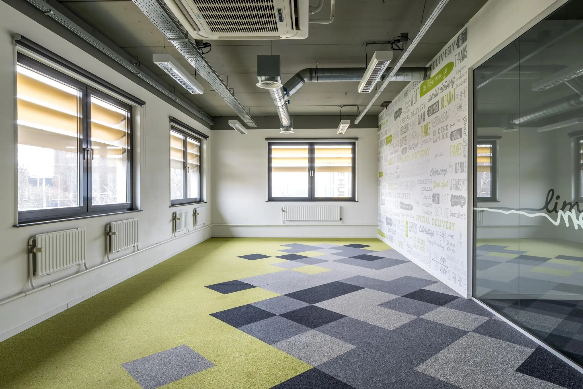 Modern kantoorinterieur aan de Laarderhoogtweg met kleurrijke tapijttegels, grote ramen en een glazen wand met grafische teksten.