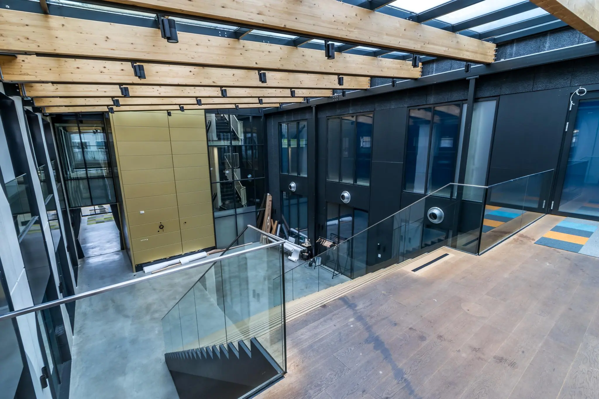 Moderne binnenruimte aan de Laarderhoogtweg met glazen balustrades, houten plafondbalken en een industriële afwerking.