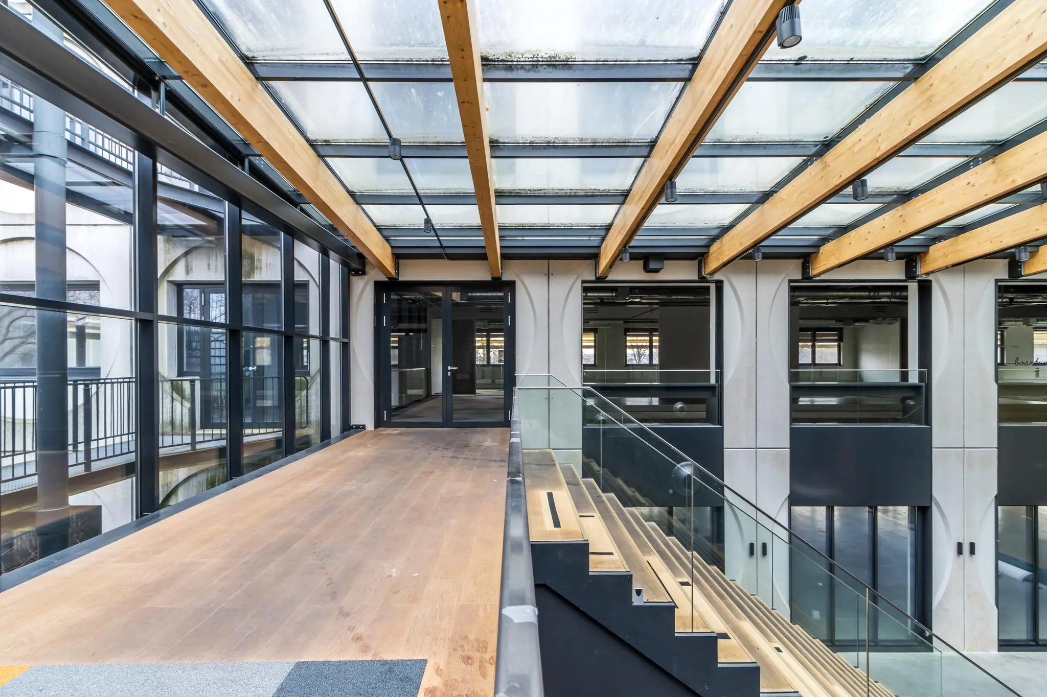 Modern interieur van een kantoorpand aan de Laarderhoogtweg met glazen dak, houten loopbrug en open trappenhuis.