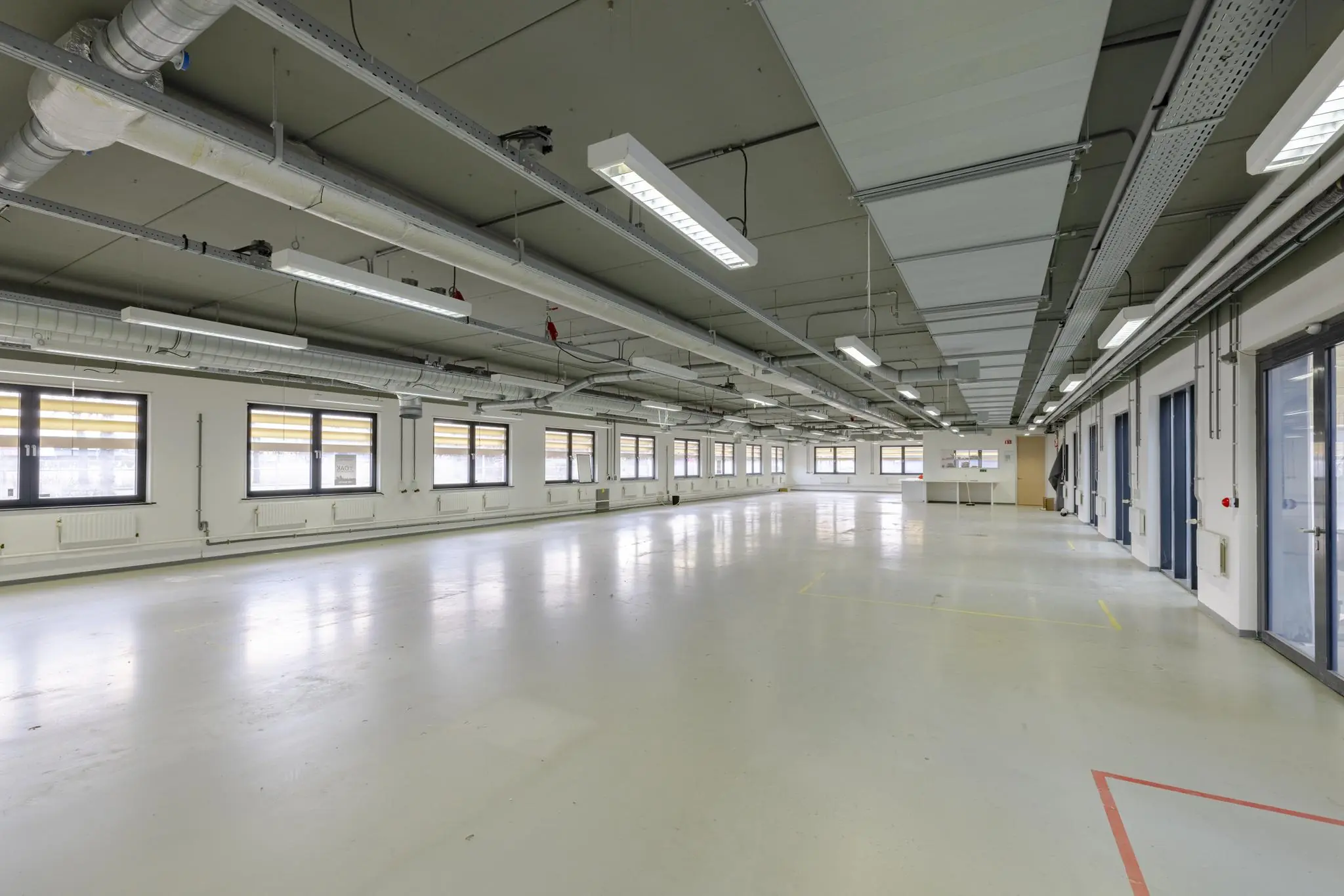 Ruime, lege industriële verdieping aan de Laarderhoogtweg met ramen, systeemplafond en zichtbare ventilatiebuizen.