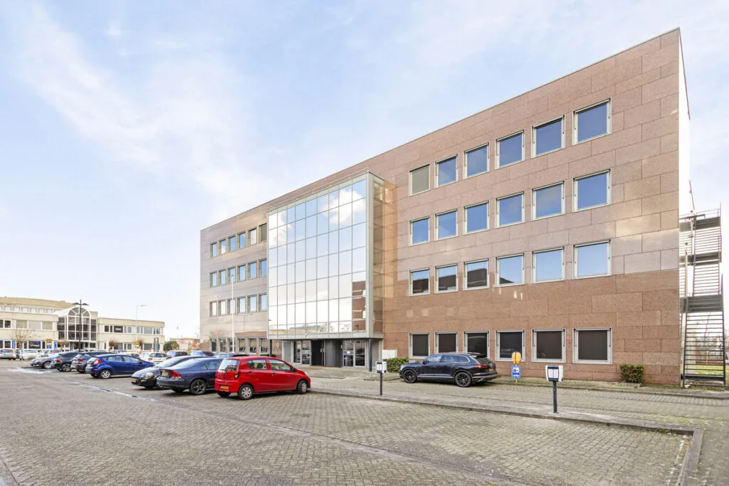 Kantoorgebouw aan de Curieweg met parkeerplaatsen aan de voorzijde, gezien op een zonnige dag.