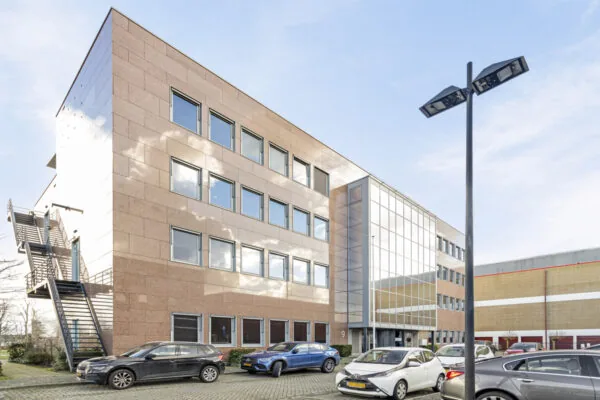 Modern kantoorgebouw aan de Curieweg met parkeerplaatsen en een externe trap aan de zijkant.