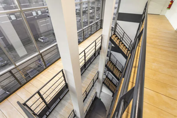Binnenaanzicht van het trappenhuis en de galerijen van een modern kantoorgebouw aan de Curieweg, met grote ramen en metalen balustrades.