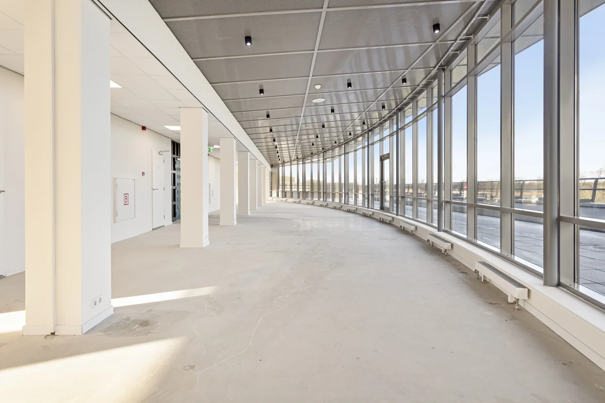 Lichte, lege kantoorruimte aan de Curieweg met grote ramen en een gebogen glazen gevel.