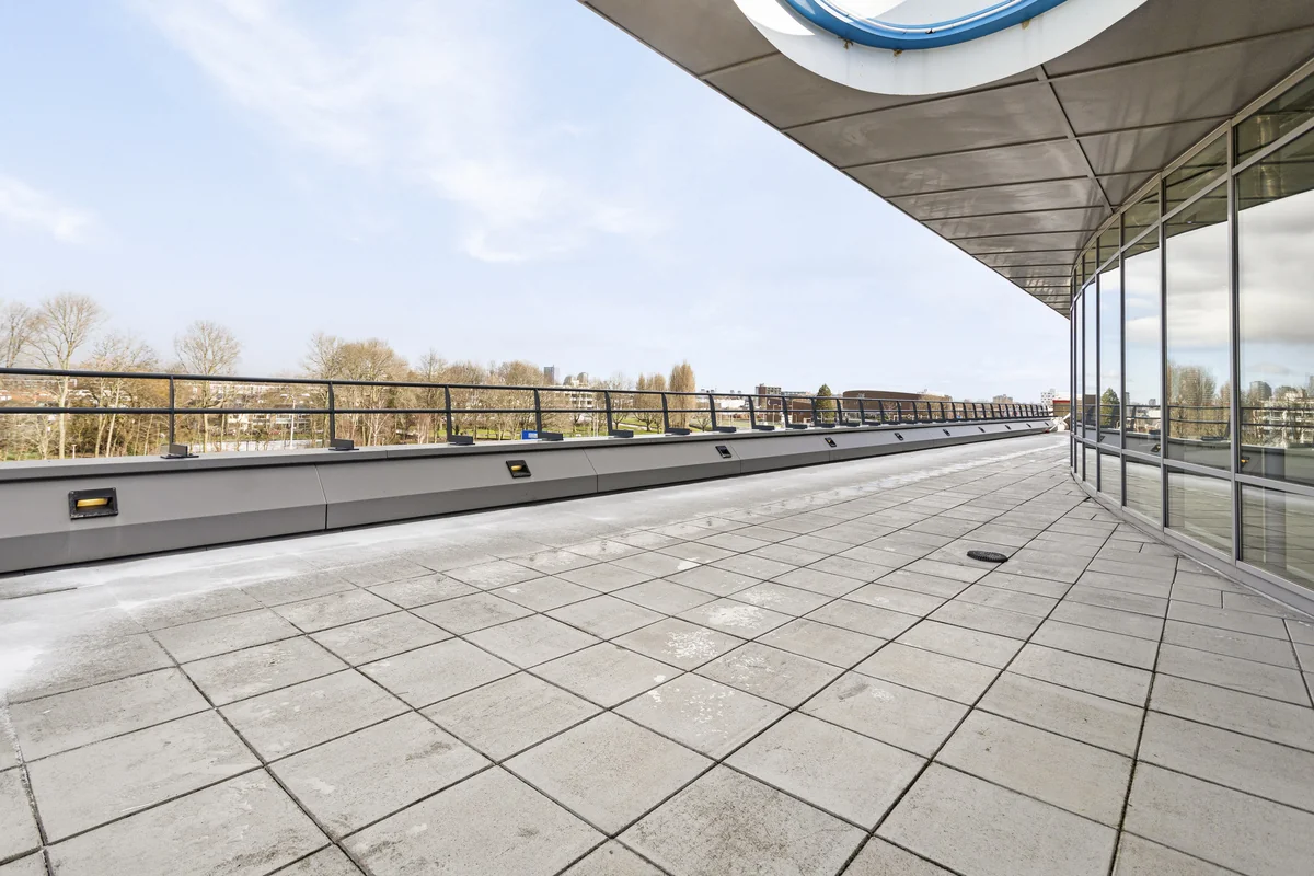 Ruim betegeld dakterras met glazen gevel en uitzicht op bomen en stad bij Curieweg.