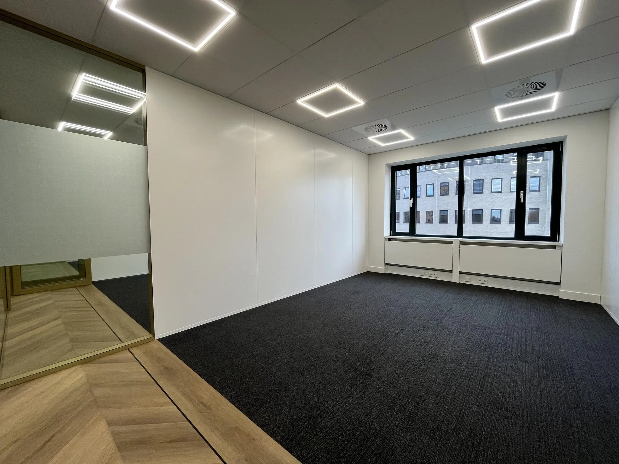 Modern, leeg kantoor aan de Euclideslaan met grote ramen, zwarte vloerbedekking en stijlvolle plafondverlichting.