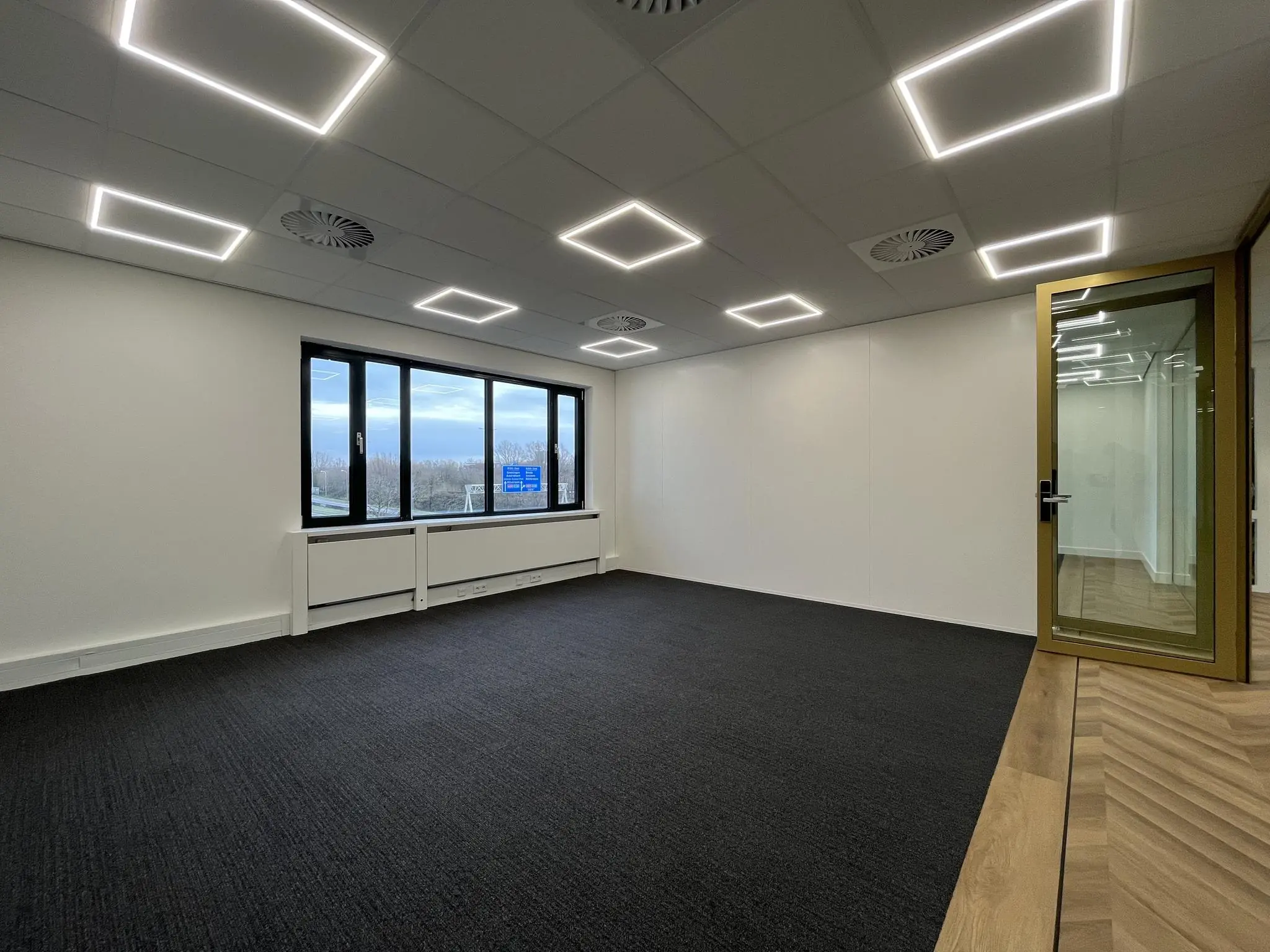 Leeg kantoor op de Euclideslaan met strak tapijt, rechthoekige LED-verlichting en glazen deur.