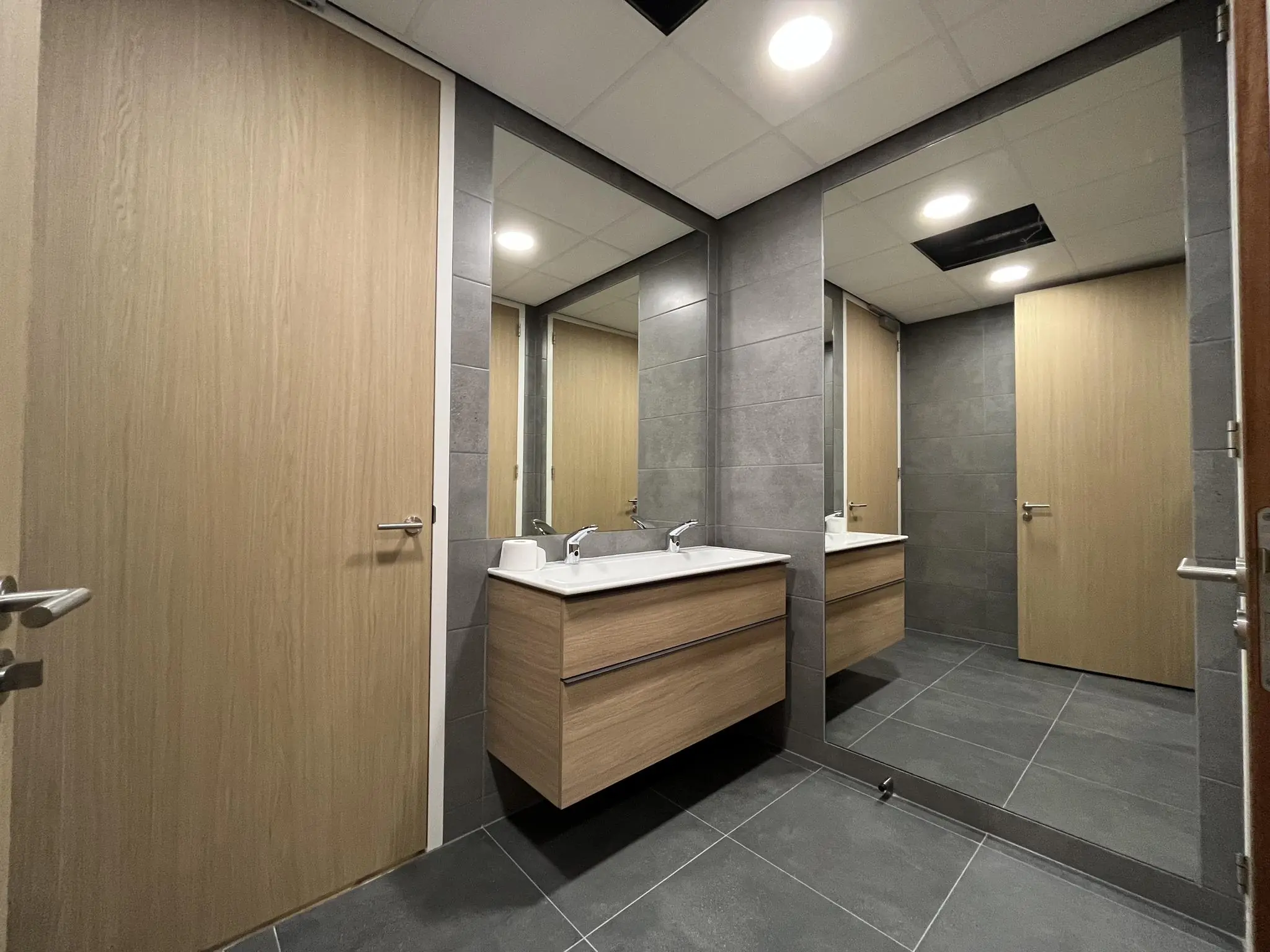 Moderne badkamer met grijze tegels, een houten wastafelmeubel met dubbele wasbak en een grote wandspiegel in een ruimte aan de Euclideslaan.