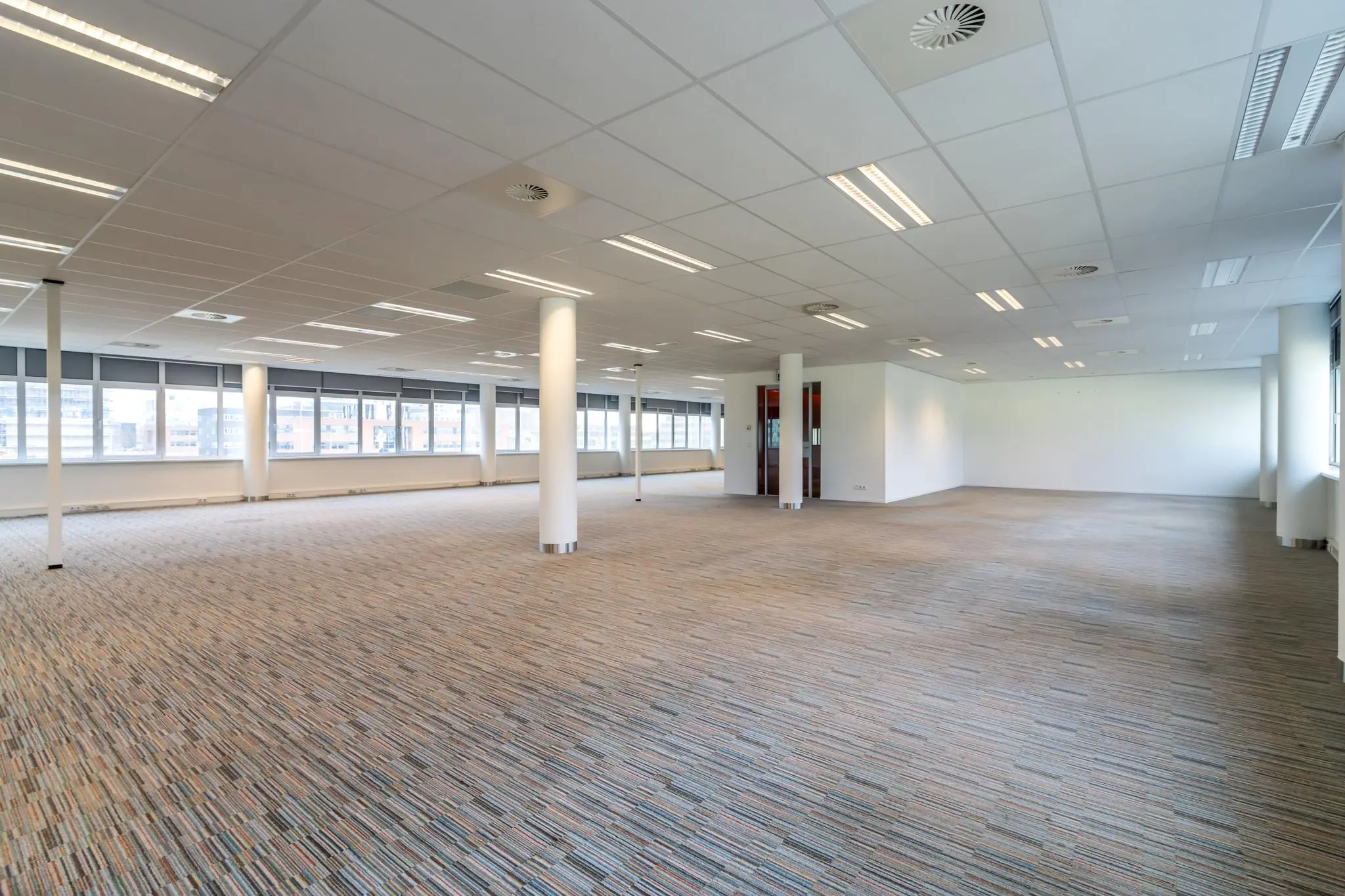Leeg en licht kantoorruimte aan de Lemelerbergweg met ramen rondom en tapijtvloer.