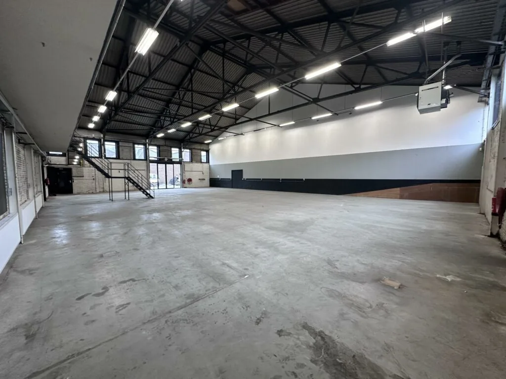 Ruime, lege bedrijfshal aan de Pilotenstraat met betonnen vloer, hoge plafonds en metalen trap.