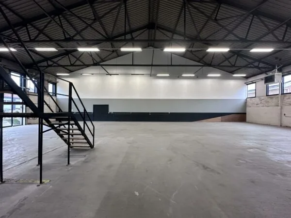 Leeg industrieel magazijn aan de Pilotenstraat met betonnen vloer, metalen trap en hoge plafonds.