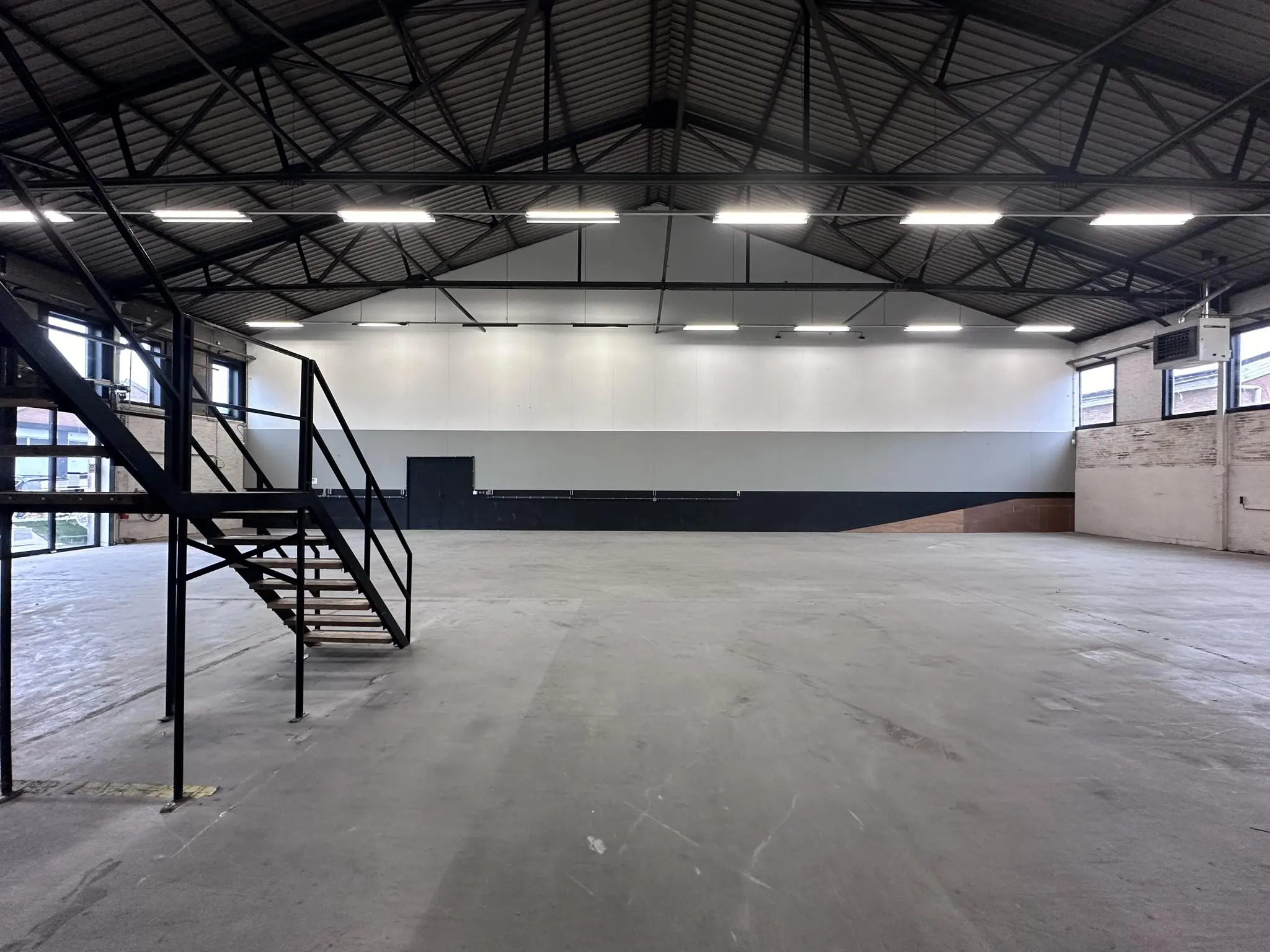 Leeg industrieel magazijn aan de Pilotenstraat met betonnen vloer, metalen trap en hoge plafonds.