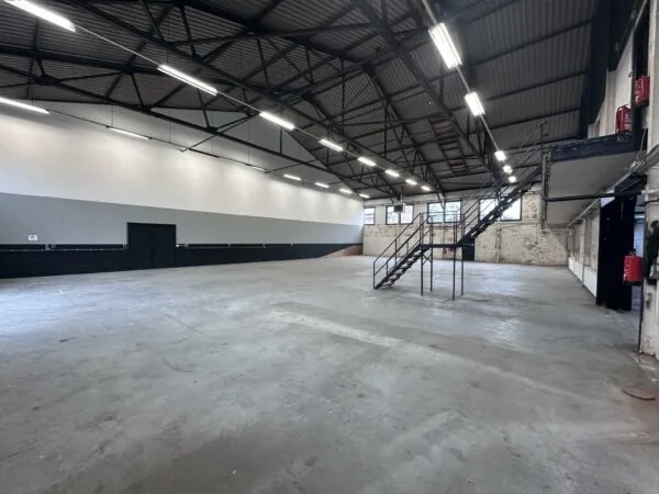 Lege industriële loods aan de Pilotenstraat met betonnen vloer, metalen trap en hoge plafonds.