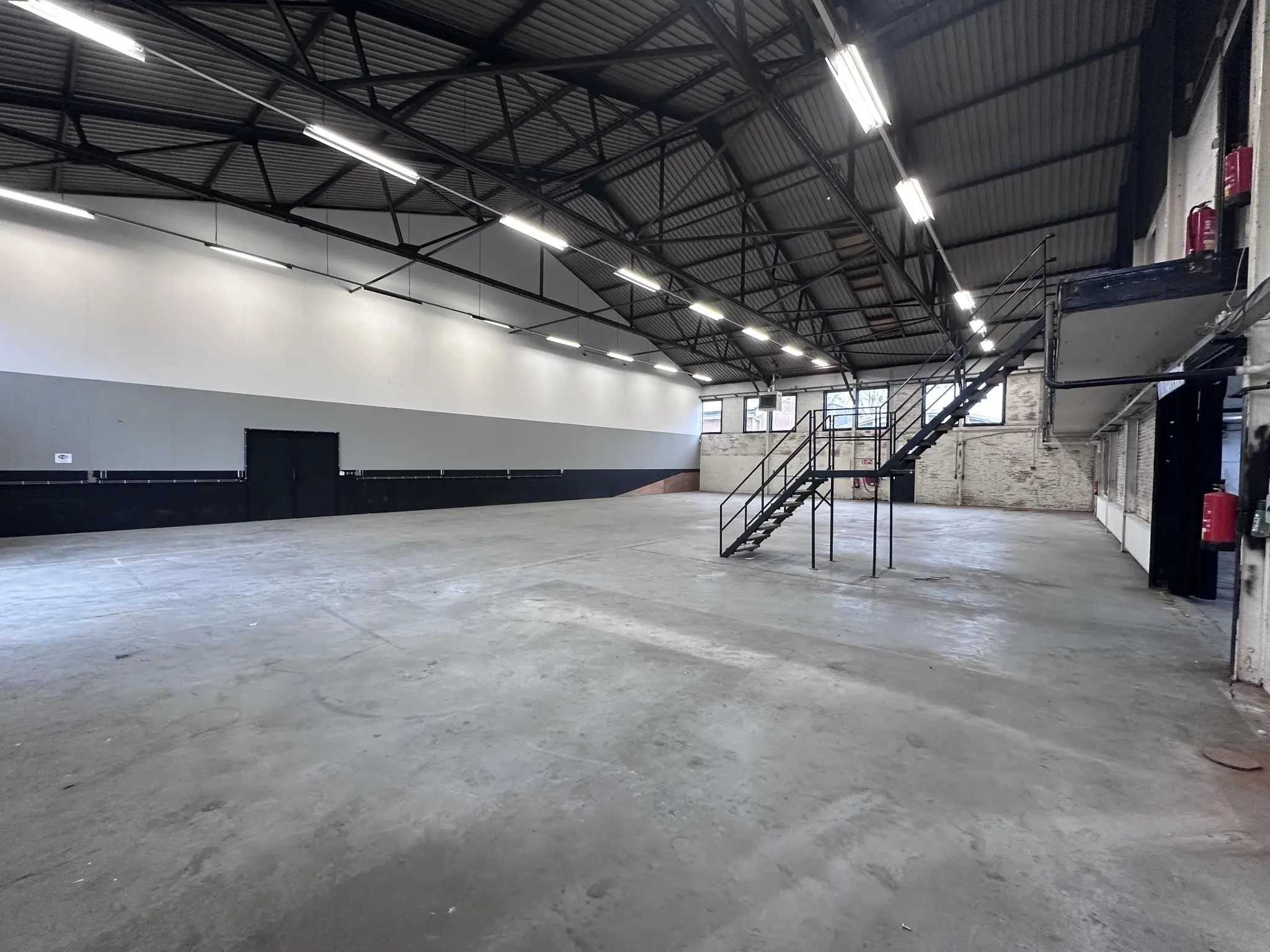Lege industriële loods aan de Pilotenstraat met betonnen vloer, metalen trap en hoge plafonds.