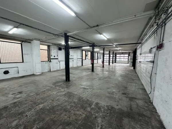 Leeg industrieel garagepand aan de Pilotenstraat met betonnen vloer en zwarte stalen palen.