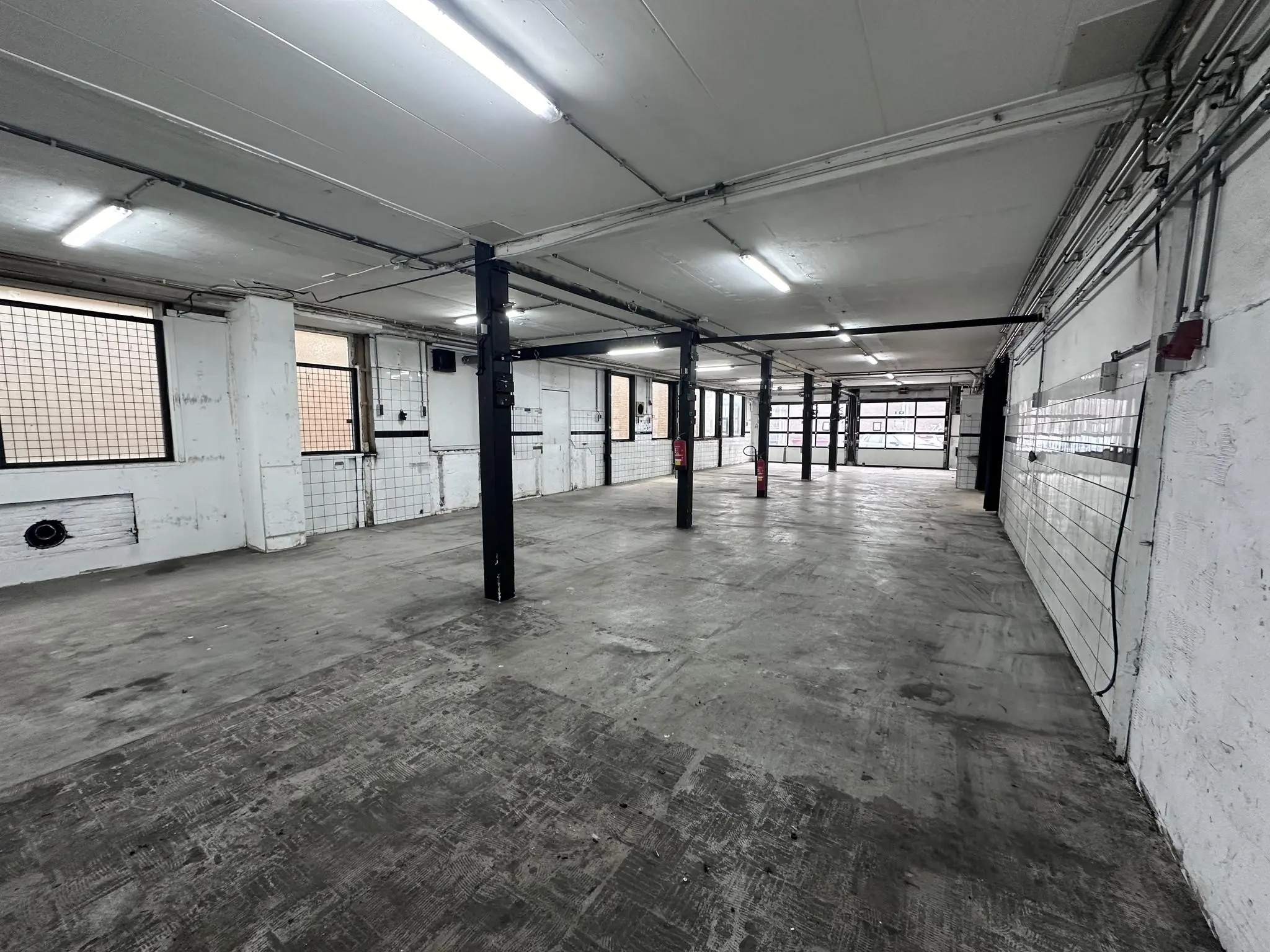 Leeg industrieel garagepand aan de Pilotenstraat met betonnen vloer en zwarte stalen palen.