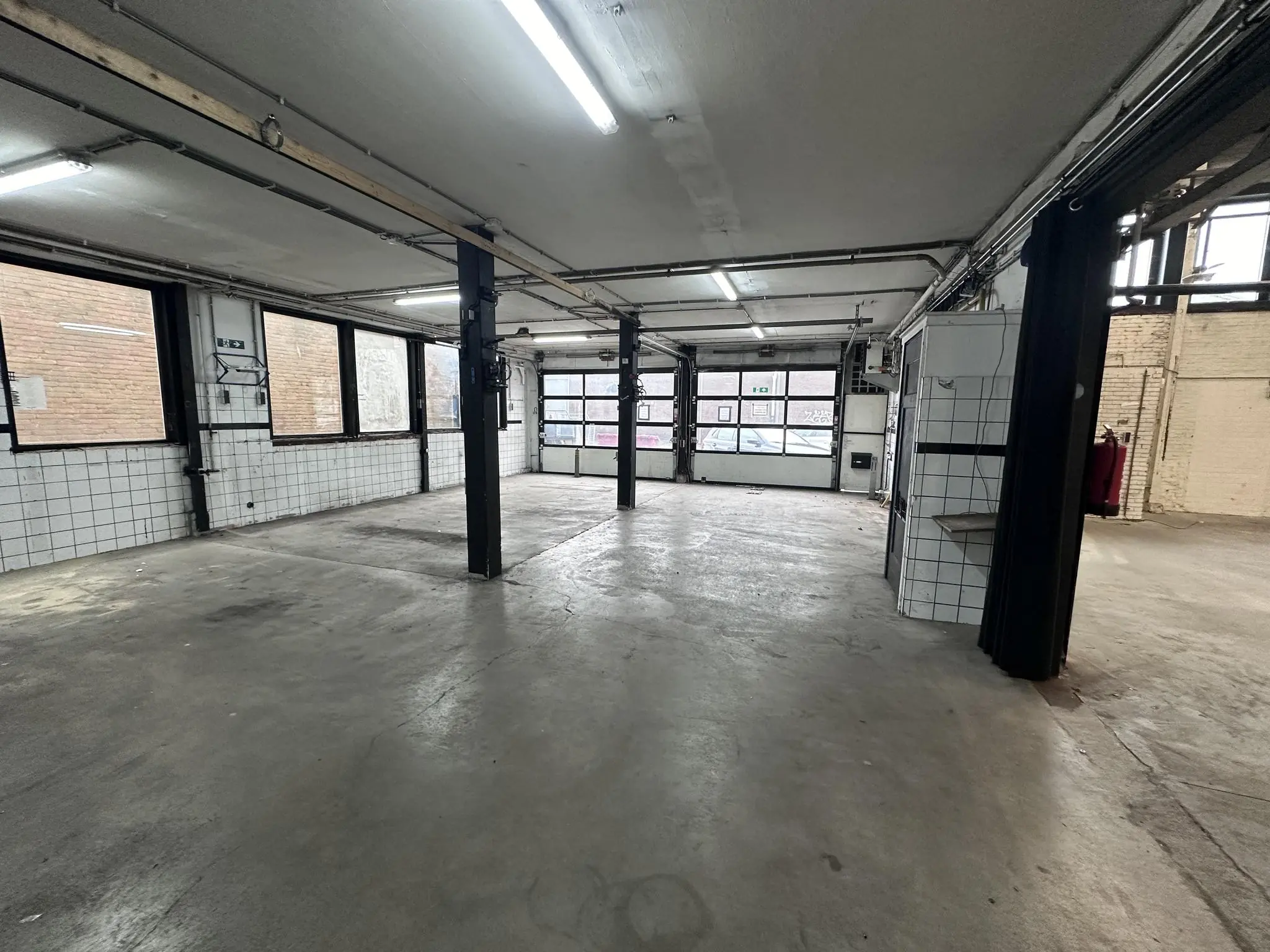 Leeg industrieel garage- of werkruimte-interieur aan de Pilotenstraat met betonnen vloer en grote ramen.