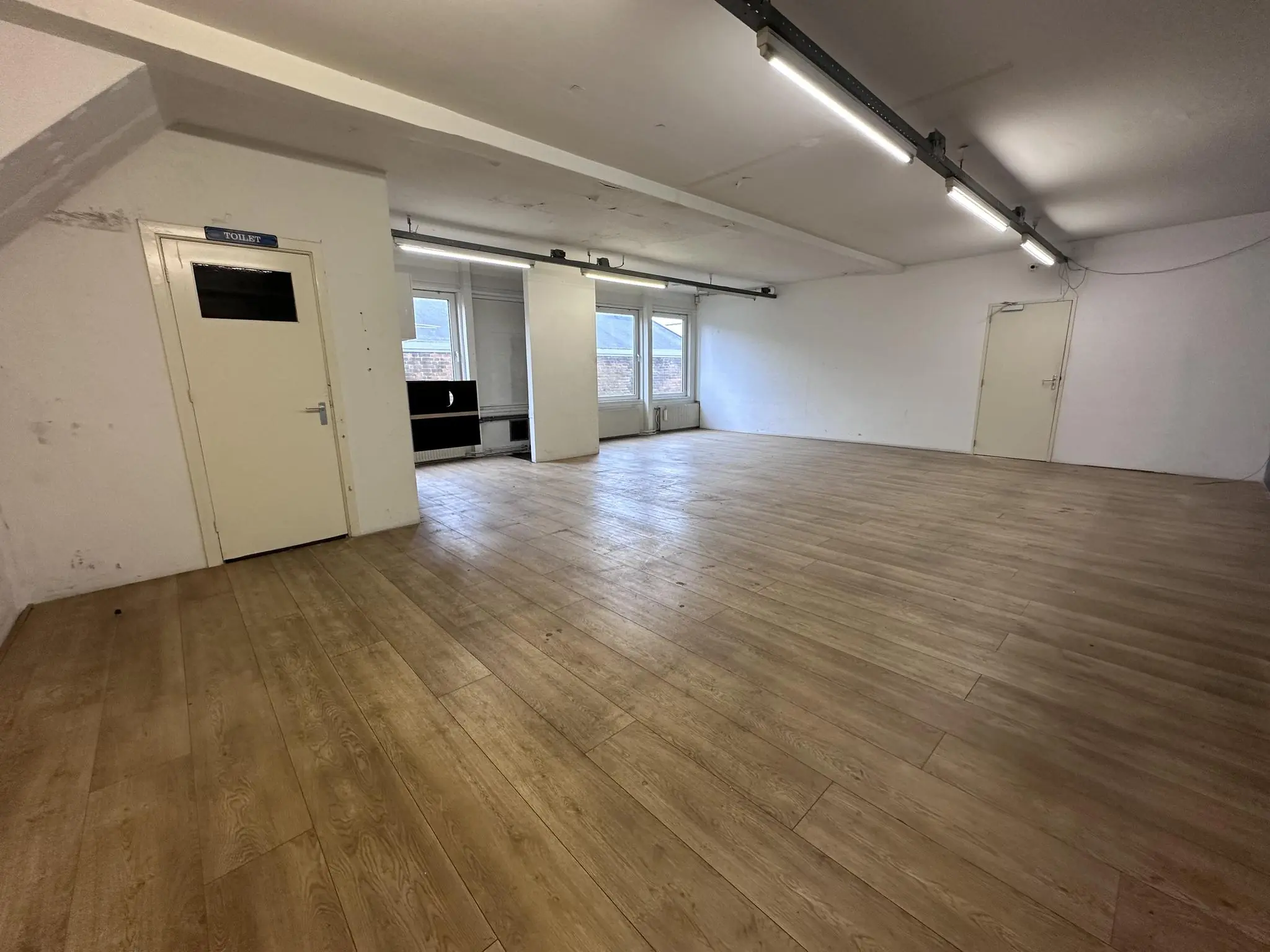 Leeg kantoor- of bedrijfsruimte aan de Pilotenstraat met houten vloer, witte muren en grote ramen.