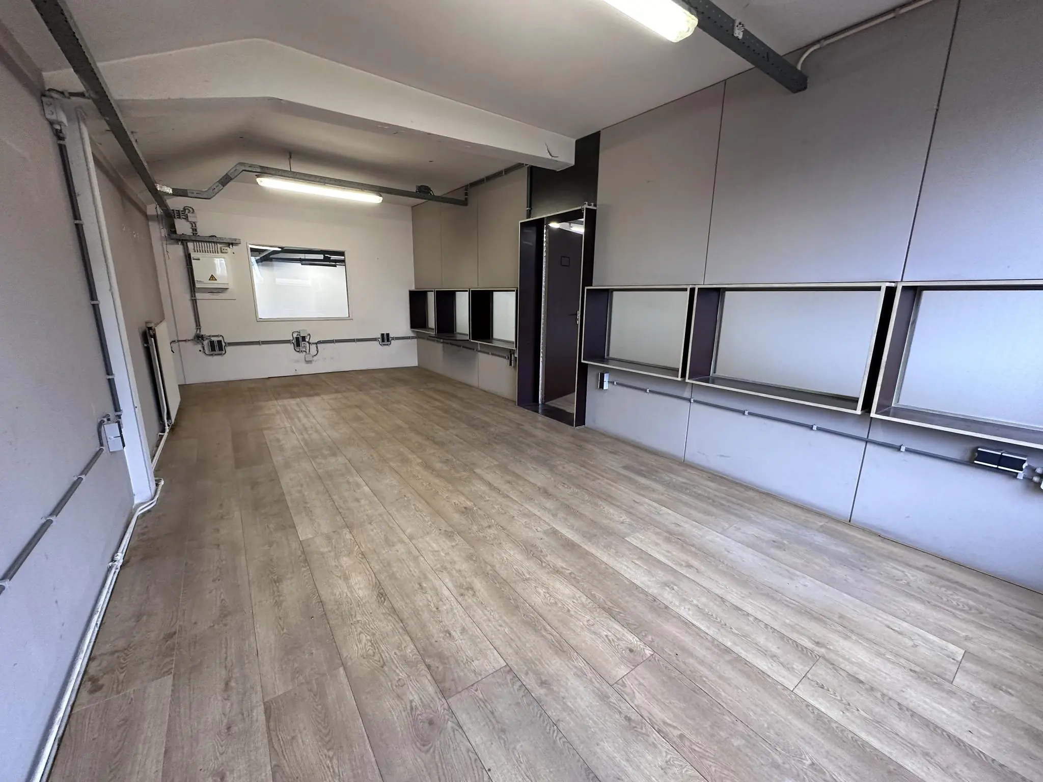 Lege kantoorruimte aan de Pilotenstraat met houten vloer, ingebouwde werkplekken en tl-verlichting.