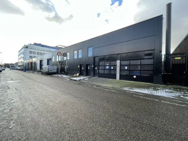 Bedrijfsgebouwen aan de Pilotenstraat met geparkeerde bus en lichte sneeuw op de stoep.