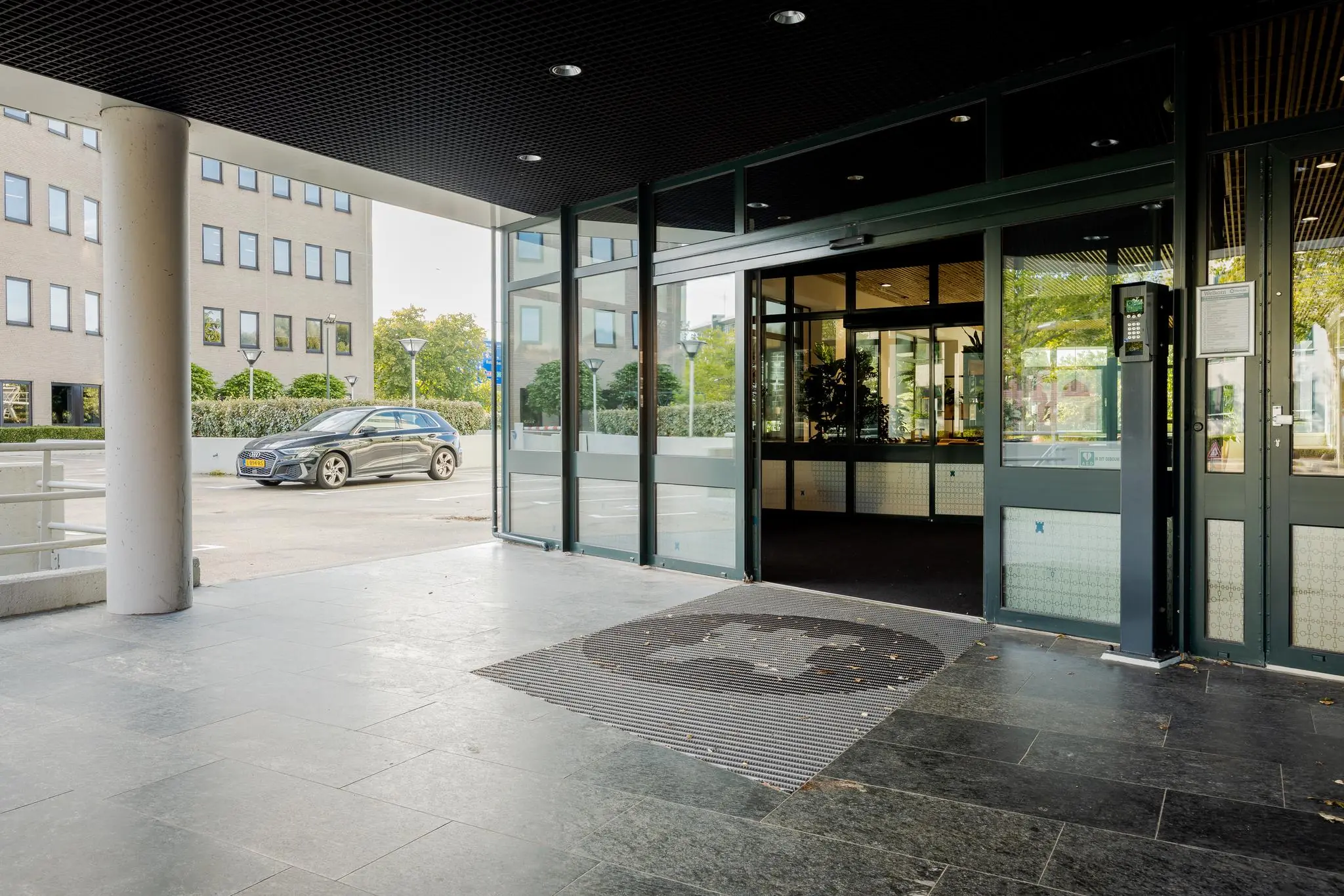Ingang van een kantoorpand aan de Euclideslaan met automatische schuifdeuren en een geparkeerde auto op de achtergrond.
