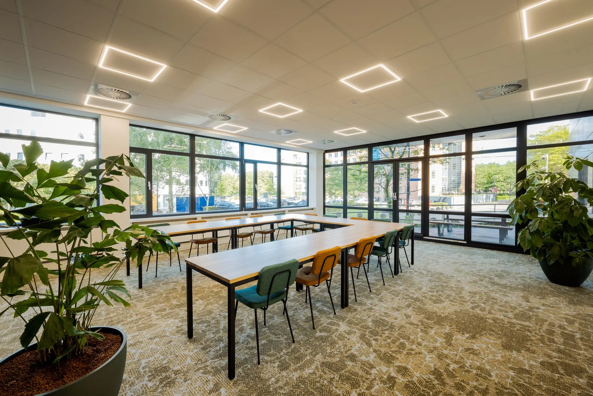 Moderne vergaderruimte aan de Euclideslaan met grote ramen, kleurrijke stoelen en veel natuurlijk licht.