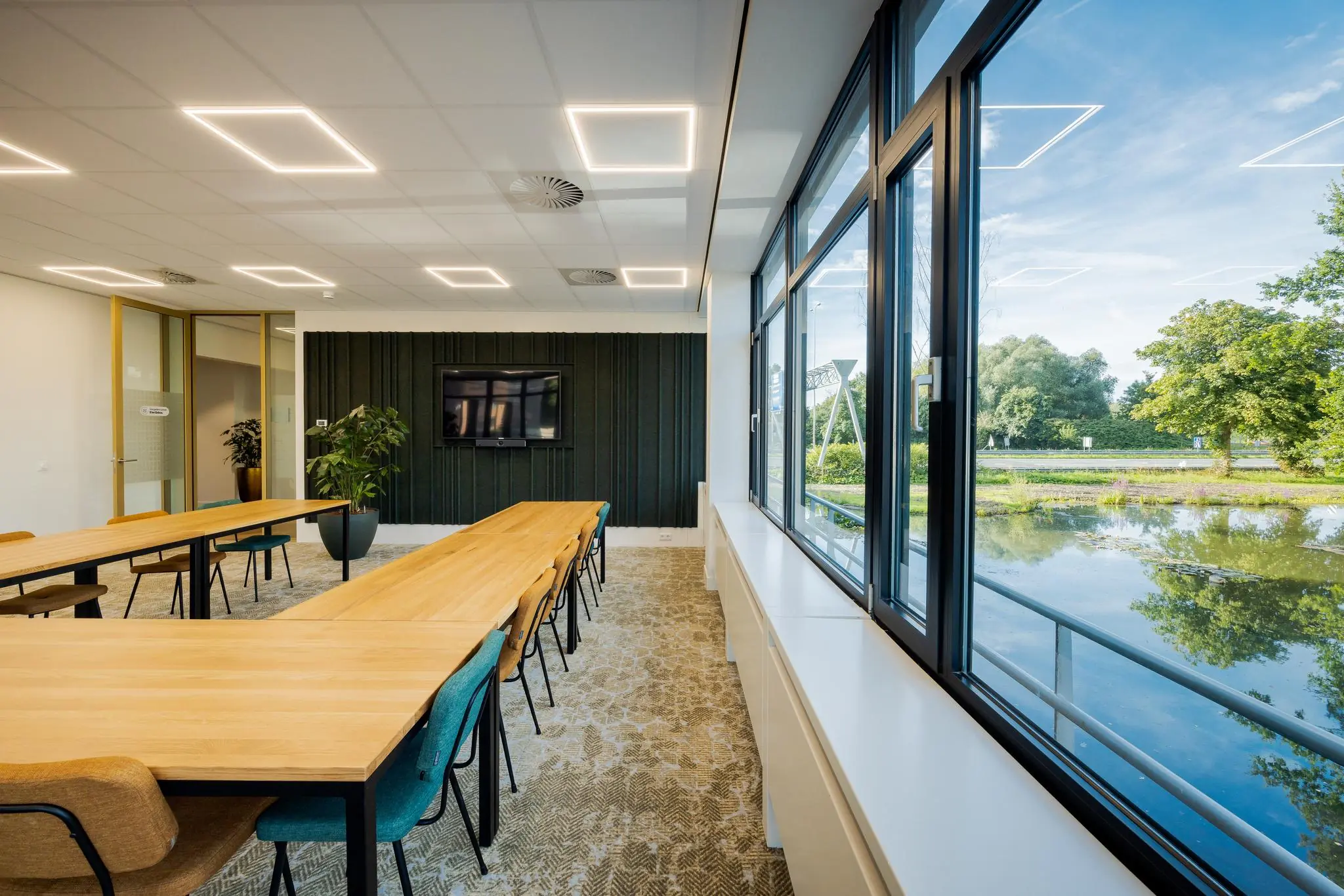 Vergaderruimte aan de Euclideslaan met moderne inrichting, lange houten tafels, grote ramen en uitzicht op een vijver en groen.