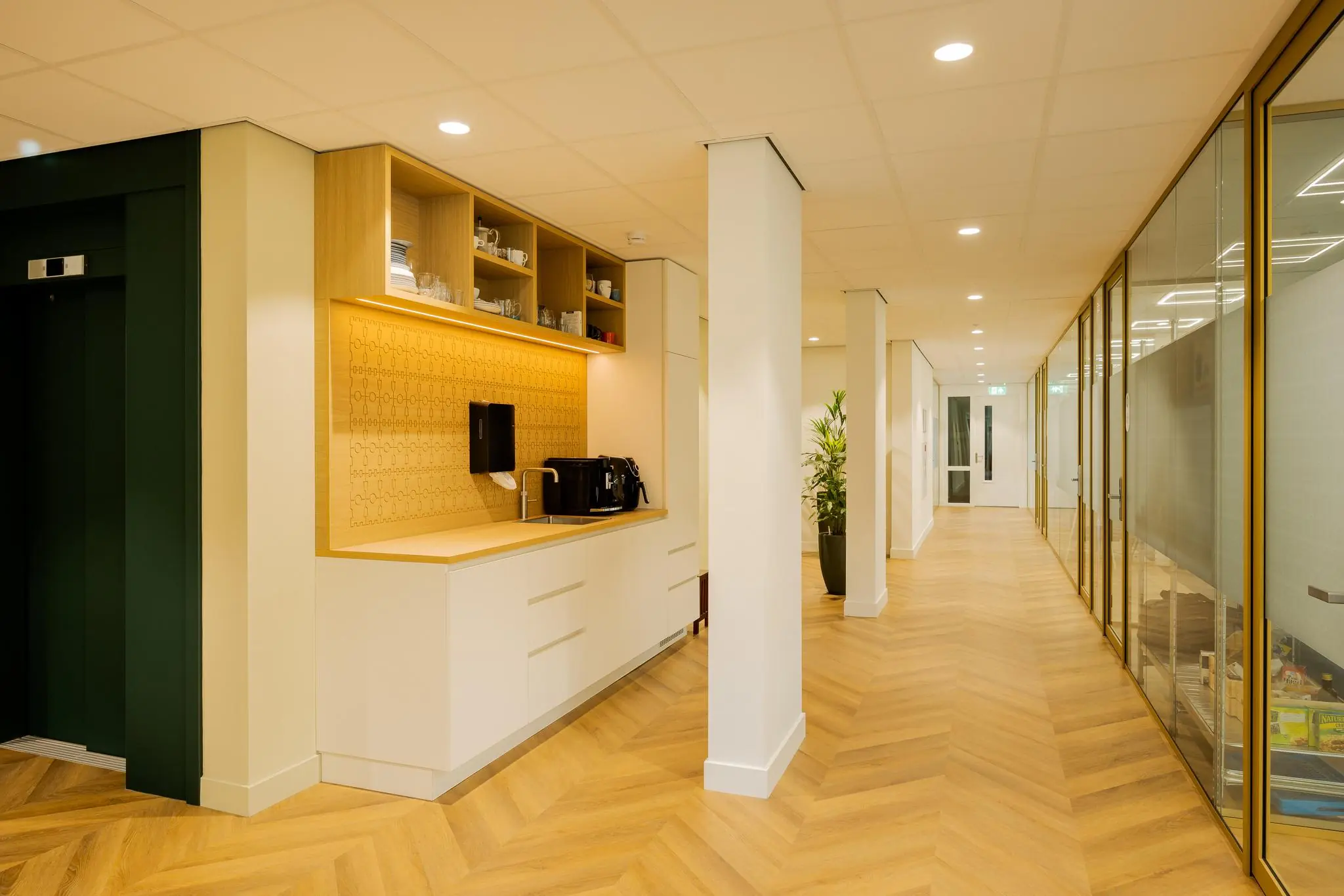 Modern kantoorinterieur aan de Euclideslaan met koffiecorner, houten vloer en glazen kantoormuren.