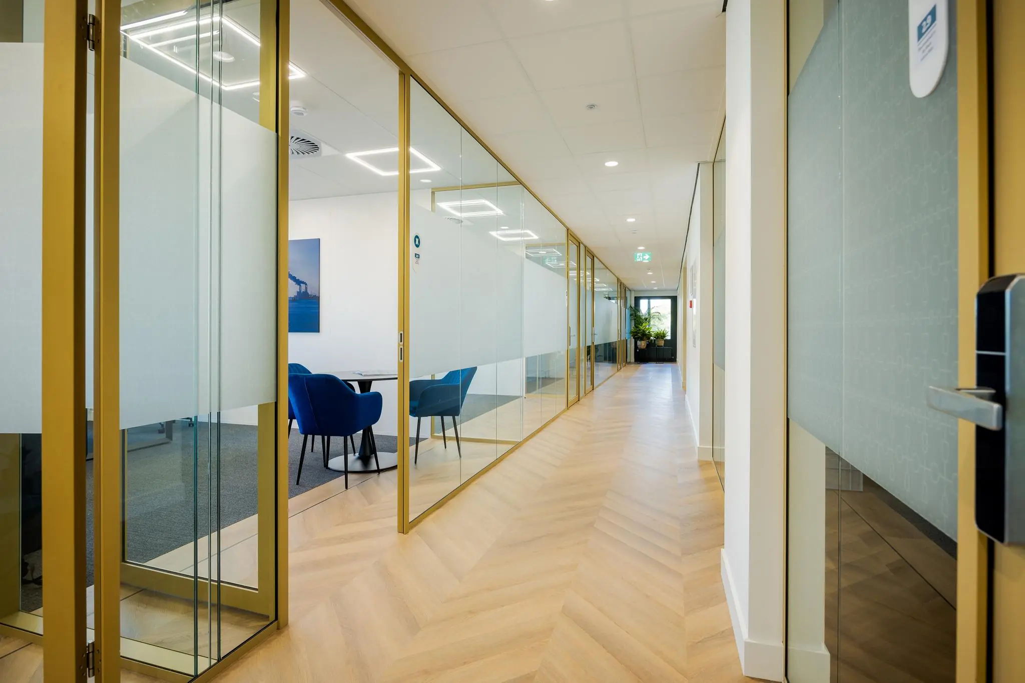 Moderne kantoorruimte aan de Euclideslaan met glazen wanden, houten visgraatvloer en blauwe stoelen in vergaderruimte.