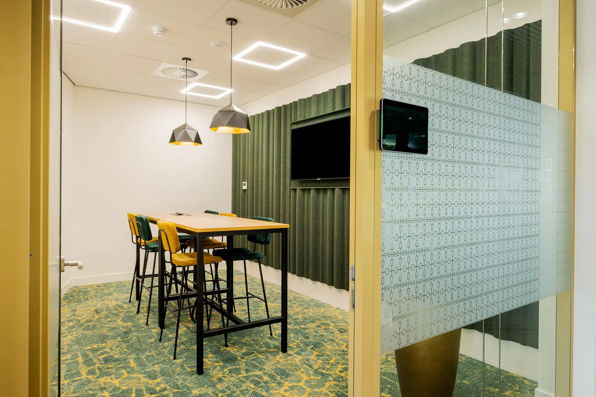 Moderne vergaderruimte aan de Euclideslaan met hoge tafel, kleurrijke stoelen en wandmonitor.