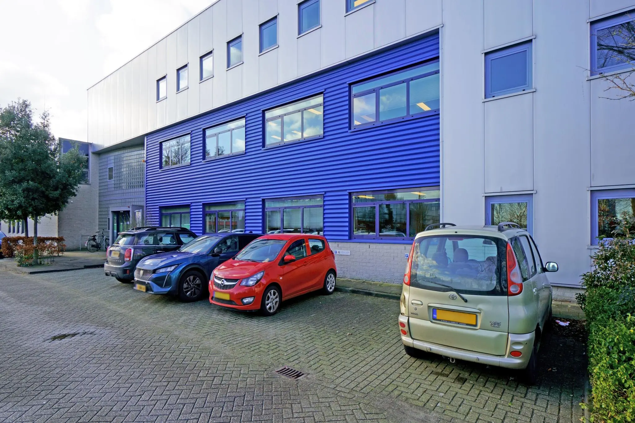Parkeerplaats met geparkeerde auto's voor een modern bedrijfspand aan de Zuiderweg.