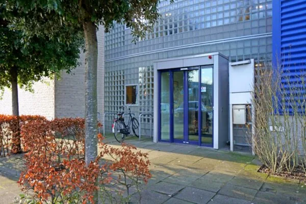 Ingang van een modern kantoorgebouw aan de Zuiderweg met glazen bouwstenen, schuifdeur en geparkeerde fiets.