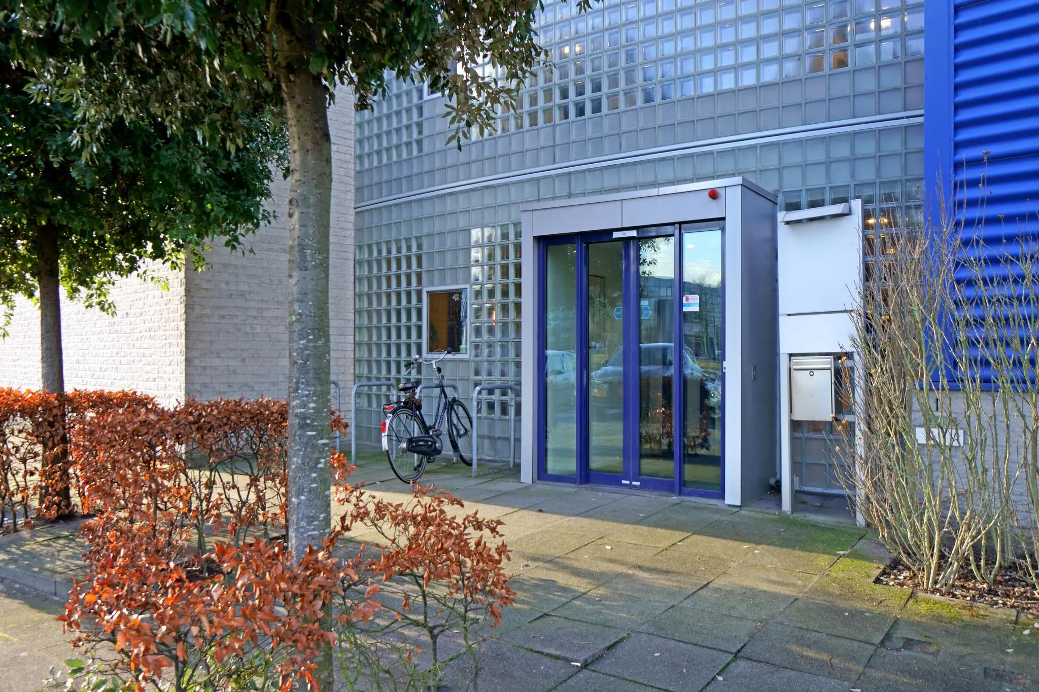 Ingang van een modern kantoorgebouw aan de Zuiderweg met glazen bouwstenen, schuifdeur en geparkeerde fiets.