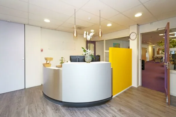 Moderne receptiebalie met gele scheidingswand en decoratieve verlichting in een kantoor aan de Zuiderweg.
